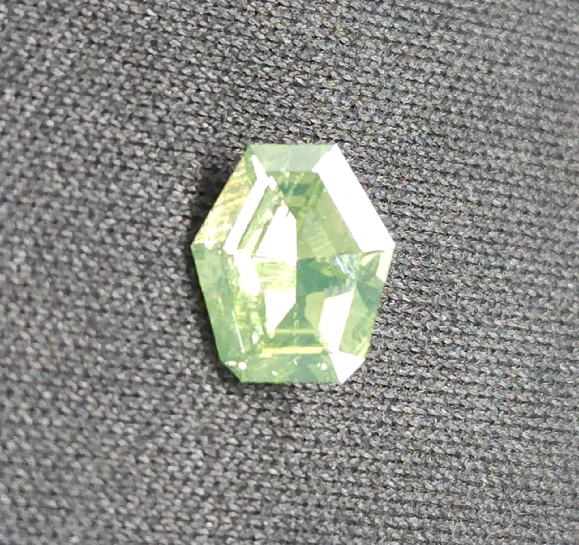 A multi-faceted gemstone with green hues placed on a textured gray surface.