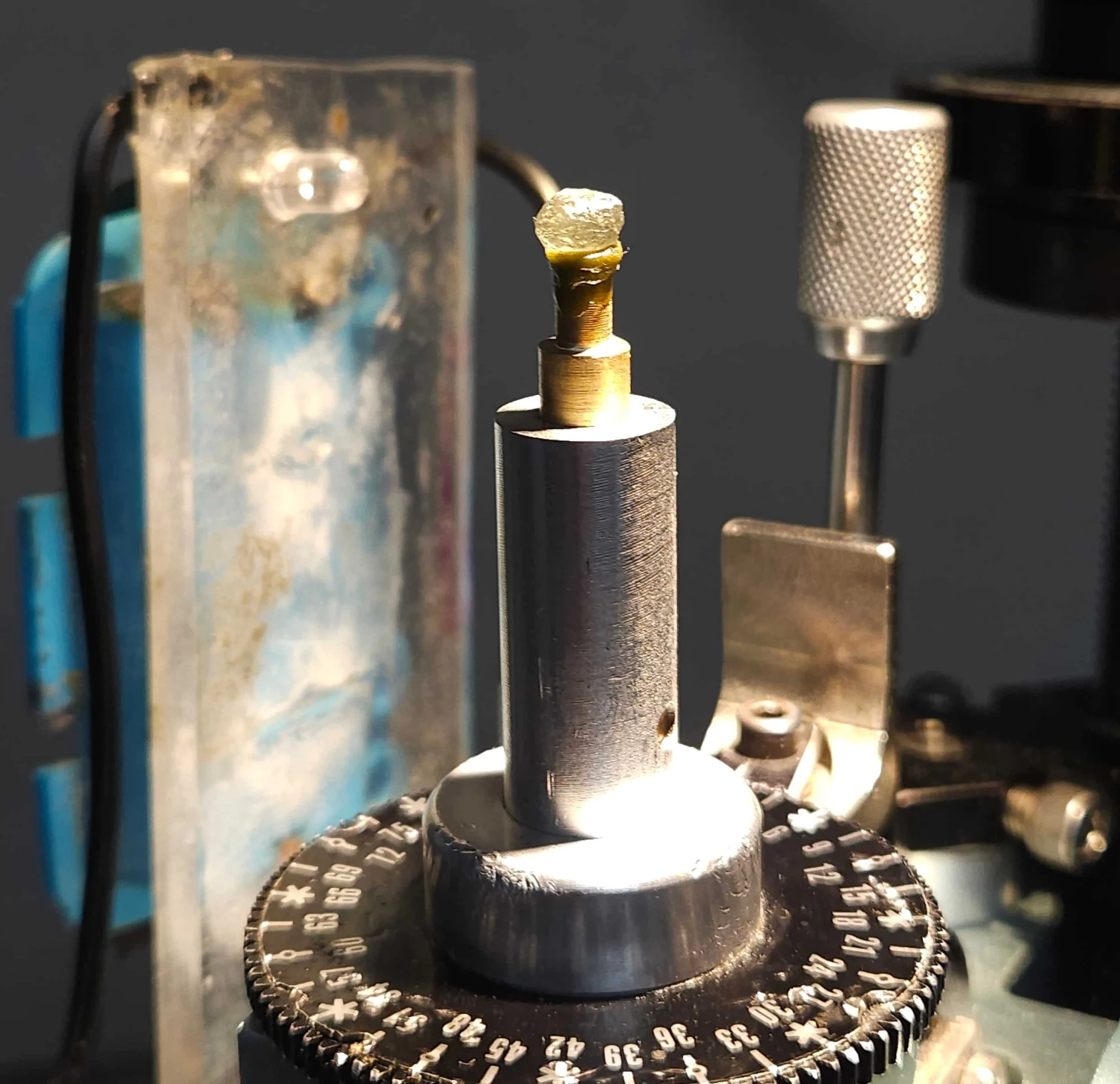 A close up of a faceting quil with a brass dop inserted holding a sapphire.