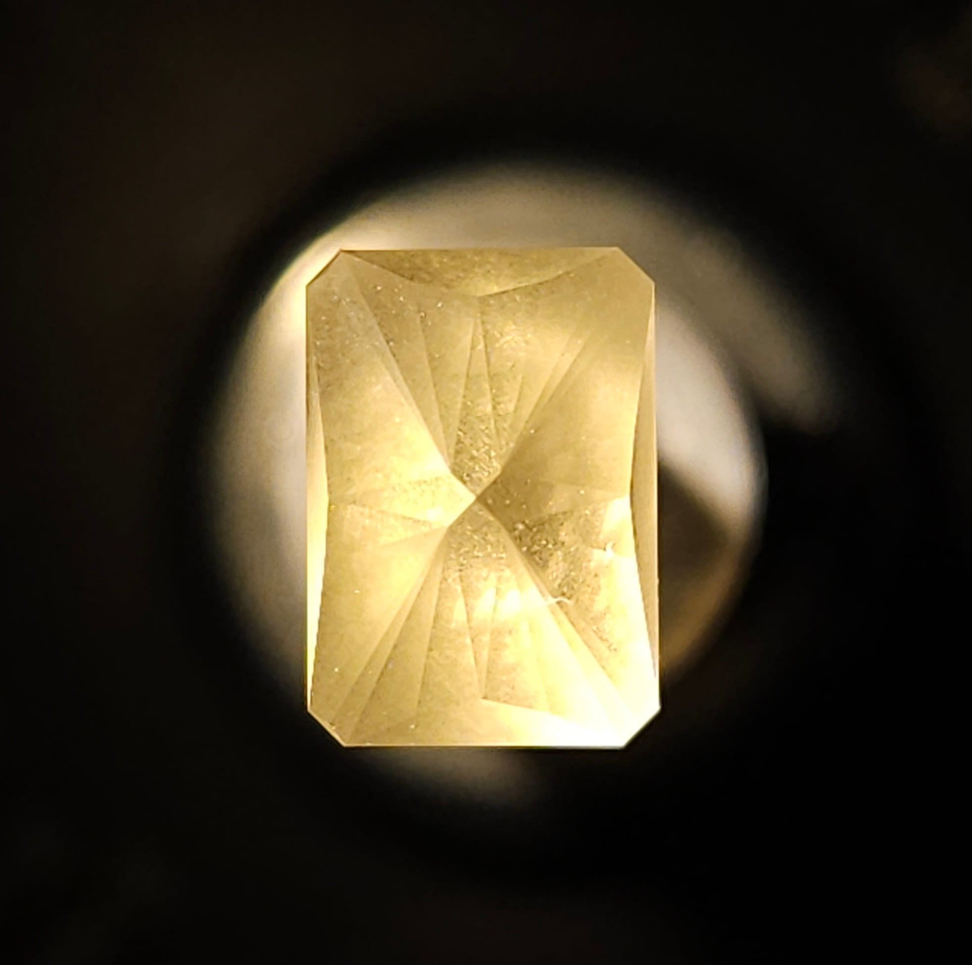 A gold-colored rectangular object with geometric patterns, viewed through a circular shadow or frame, illuminated from above.