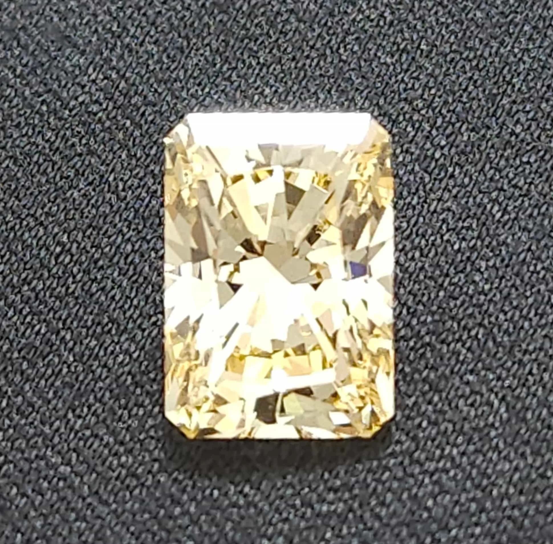 Close-up image of a sparkling, rectangular surface reflecting light, surrounded by a textured, speckled, dark background.