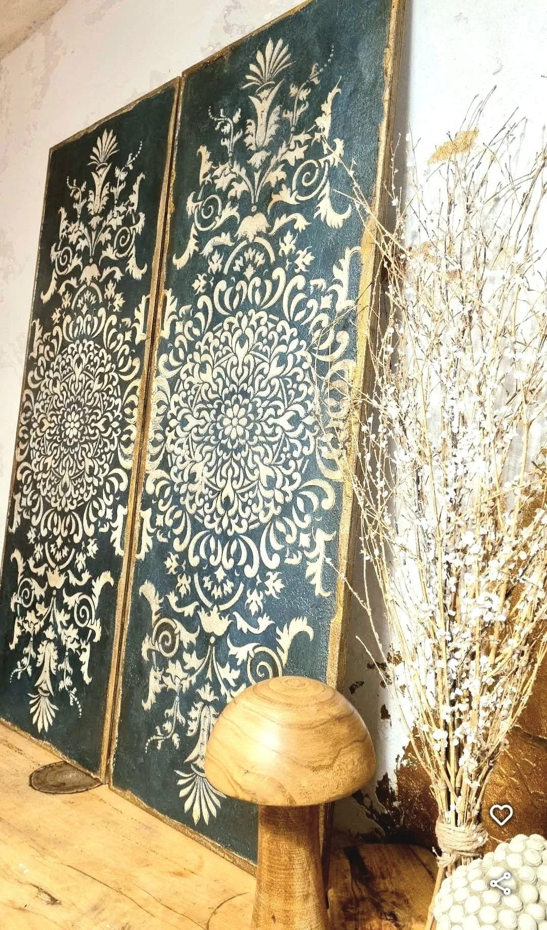 Decorative wall art featuring intricate white floral patterns on dark blue panels, a small wooden mushroom-shaped decor, and a bundle of dried white flowers tied with a string.