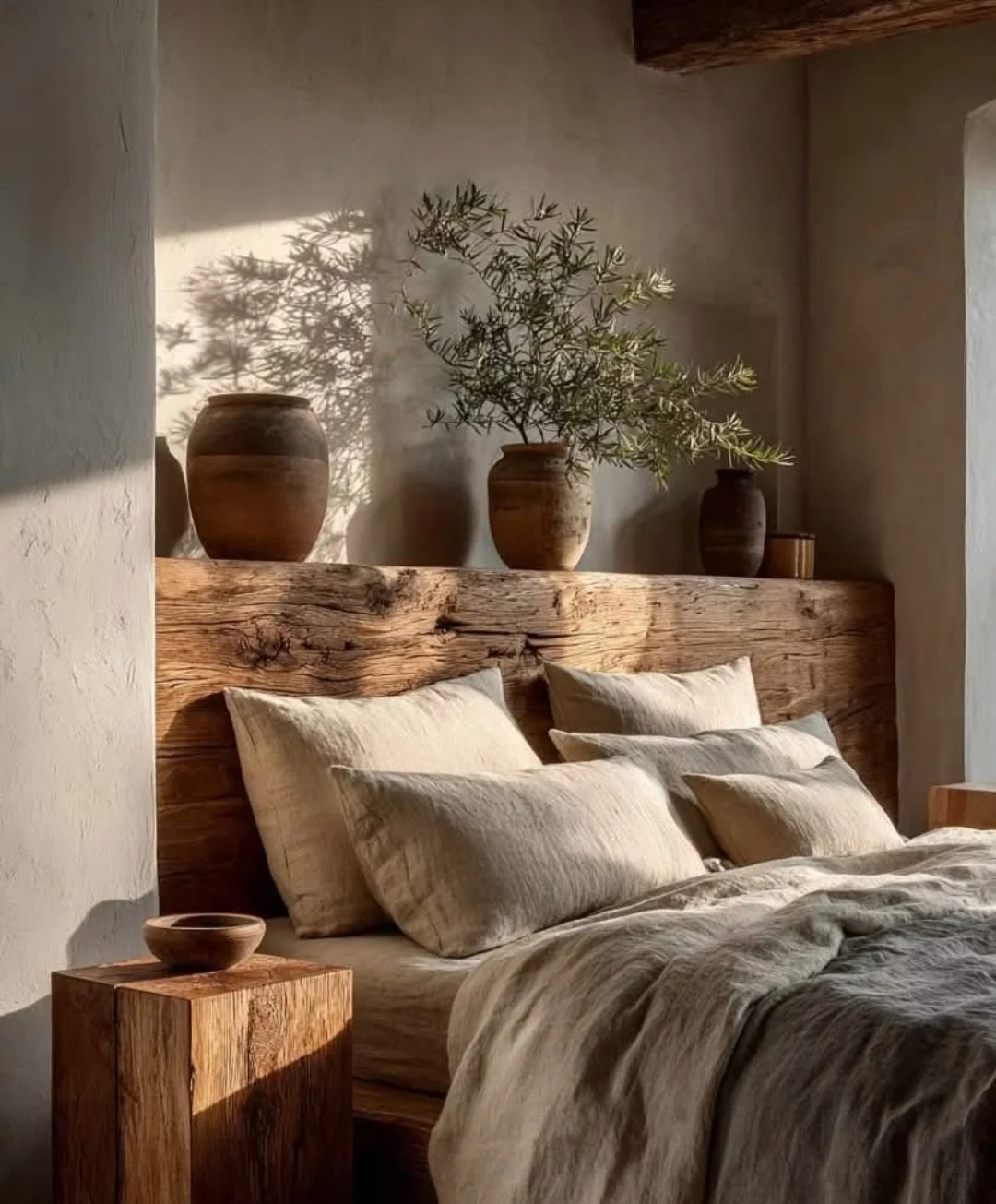 venetian plaster concrete effect wall with wooden headboard and soft linen cushions and clay plant pots.