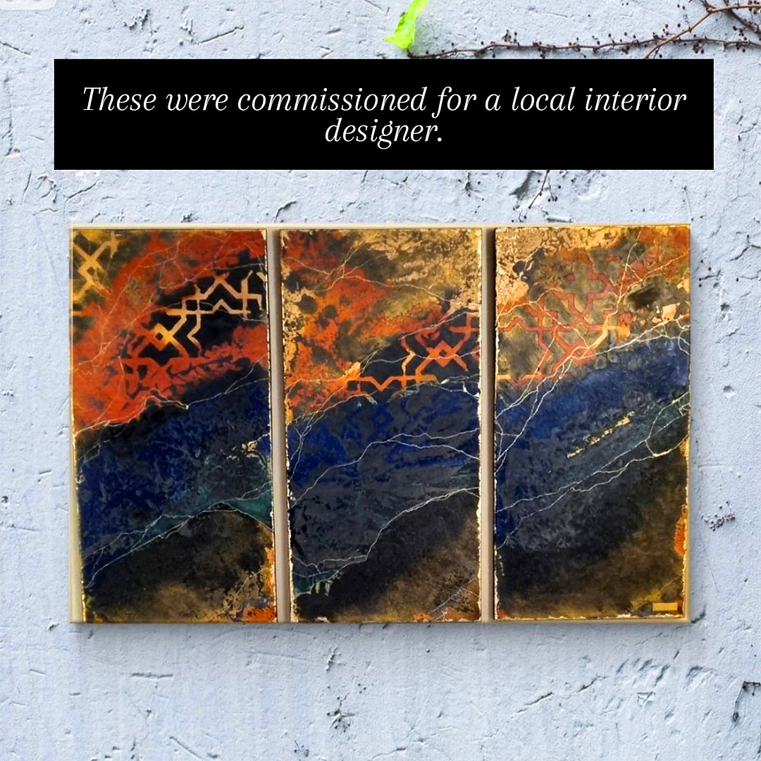 Triptych abstract artwork with black, orange, red, gold, and dark blue colors, featuring geometric and organic patterns, mounted on a white textured wall.