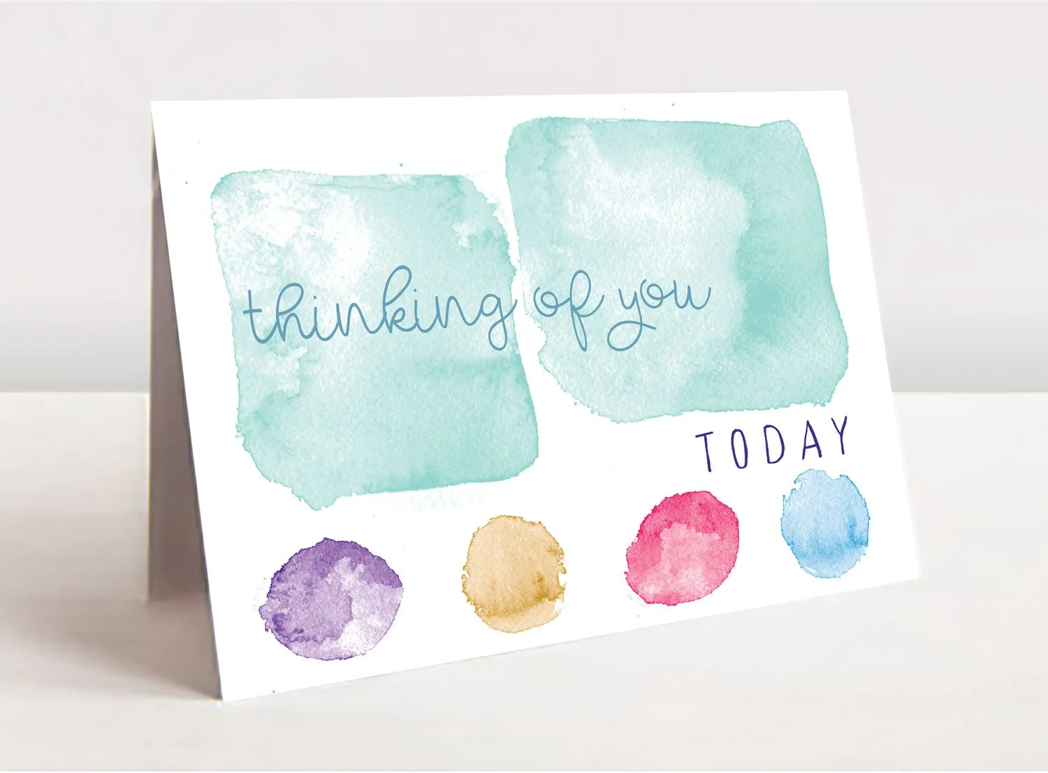 Greeting card mockup of soft watercolor squares and circles with the the text saying "thinking of you today". Two offset green squares on top and four circles along the bottom, purple, light brown, red, and green