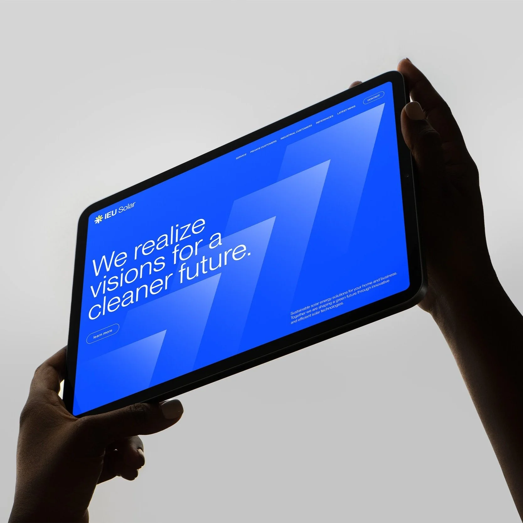 Nahaufnahme eines dunkelhautigen Menschen, der ein Tablet in der Hand hält, auf dem eine Webseite mit der Botschaft "We realizevisions for a cleaner future" angezeigt wird, vor einem hellgrauen Hintergrund.