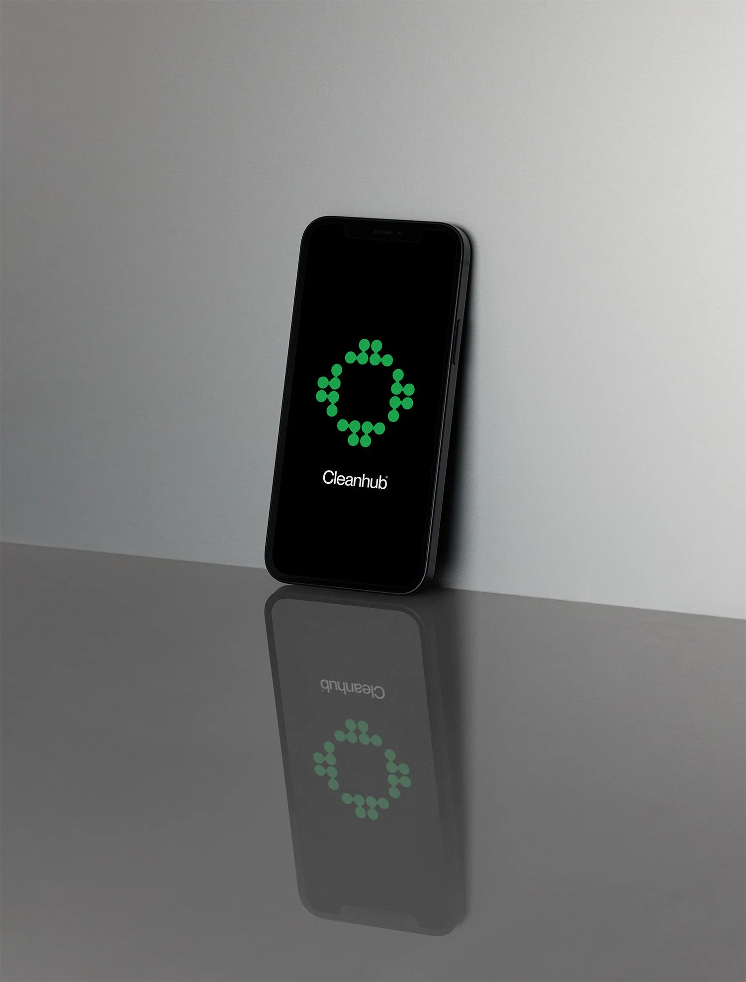 Smartphone mit der Anzeige "Cleanhub" auf dunklem Bildschirm, reflektiert auf einer glatten Oberfläche, gegen eine graue Wand im Hintergrund.
