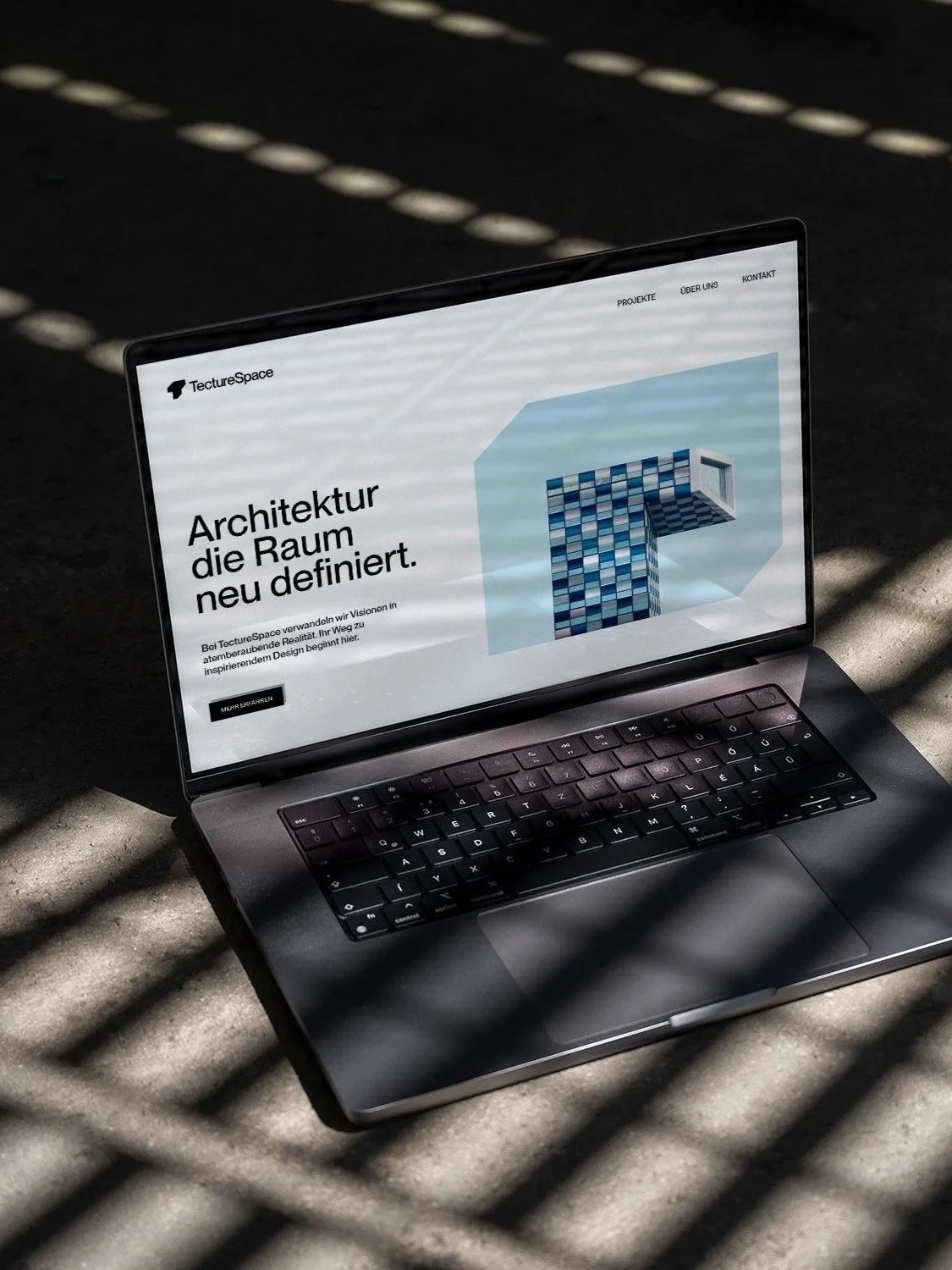 Laptop zeigt eine Webseite mit dem Titel 'Architektur, die Raum neu definiert' und einem Bild eines Blue-Cube-Gebäudes.