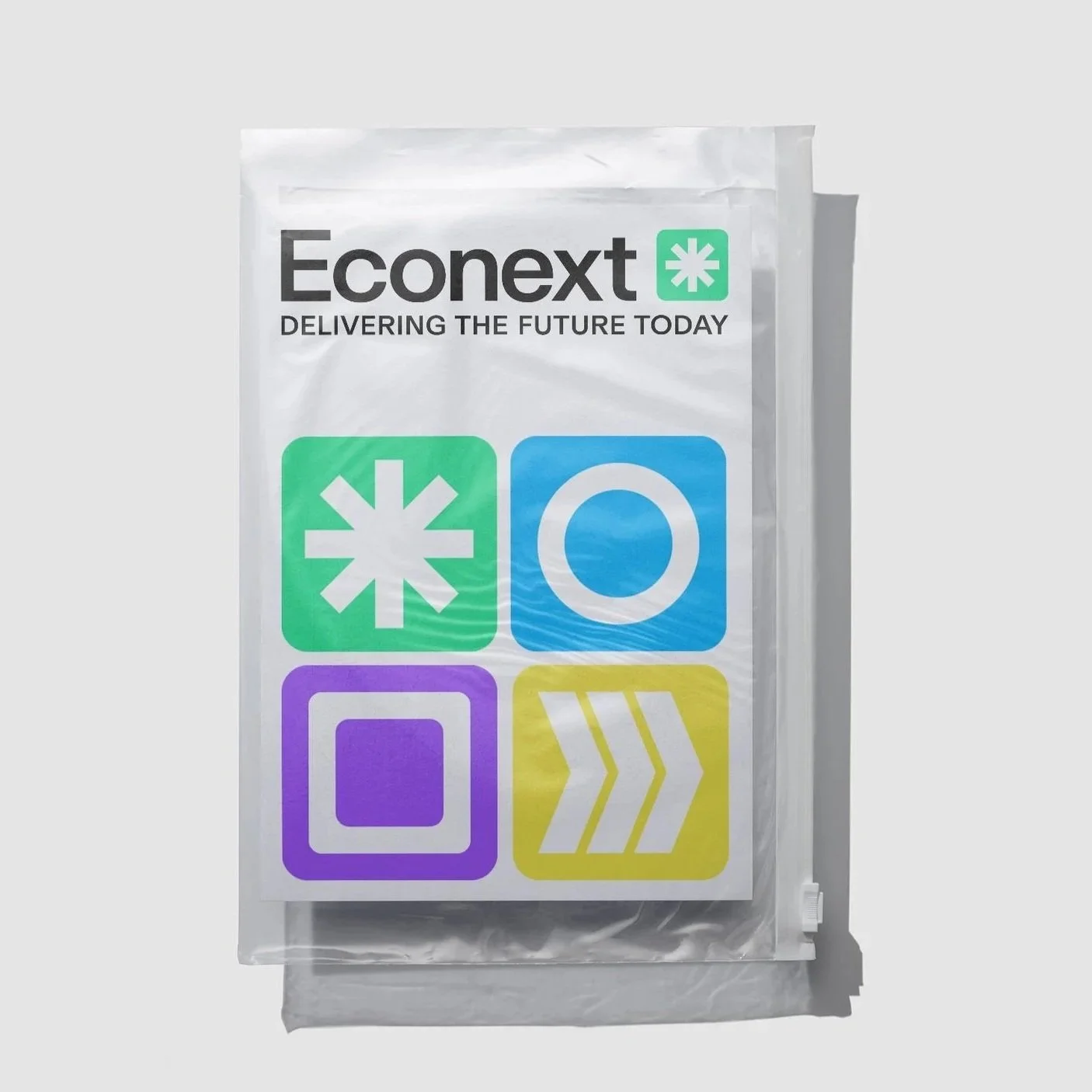 Ein transparentes Paket mit einem weißen Etikett, das das Wort 'Econext' und den Slogan 'DELIVERING THE FUTURE TODAY' anzeigt. Das Etikett hat vier farbige Symbole: eine grüne Asterisk, eine blaue Kreis, eine lilafarbene quadratische Form und eine gelbe Pfeilform.