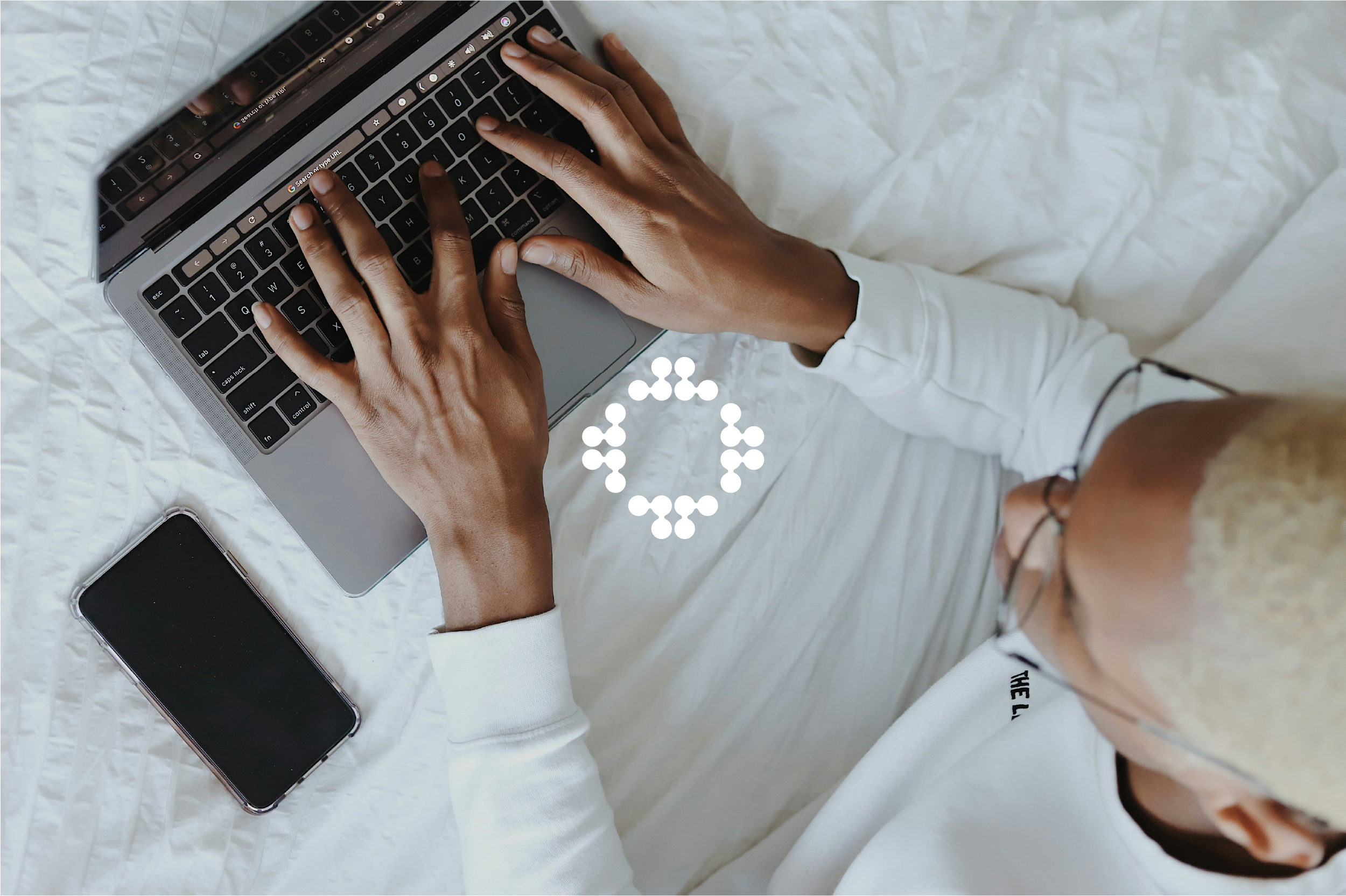 Nahaufnahme einer Person, die an einem Laptop arbeitet, mit Smartphone auf einem weißen Betttuch