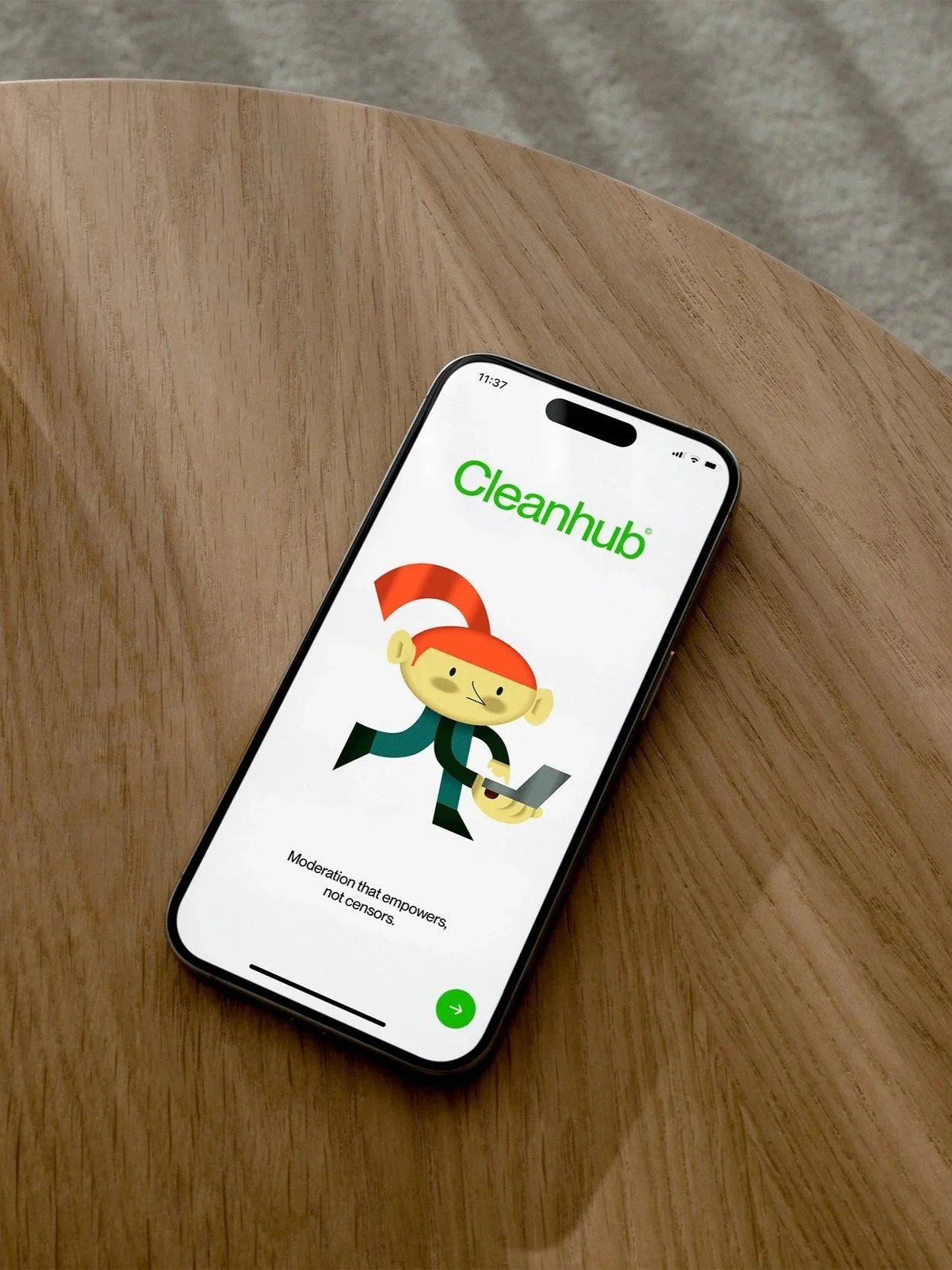 Smartphone mit Cleanhub-App auf Holzoberfläche, zeigt ein Cartoon-Mädchen mit roter Hochsteckfrisur und Laptop, im Hintergrund grauer Boden.