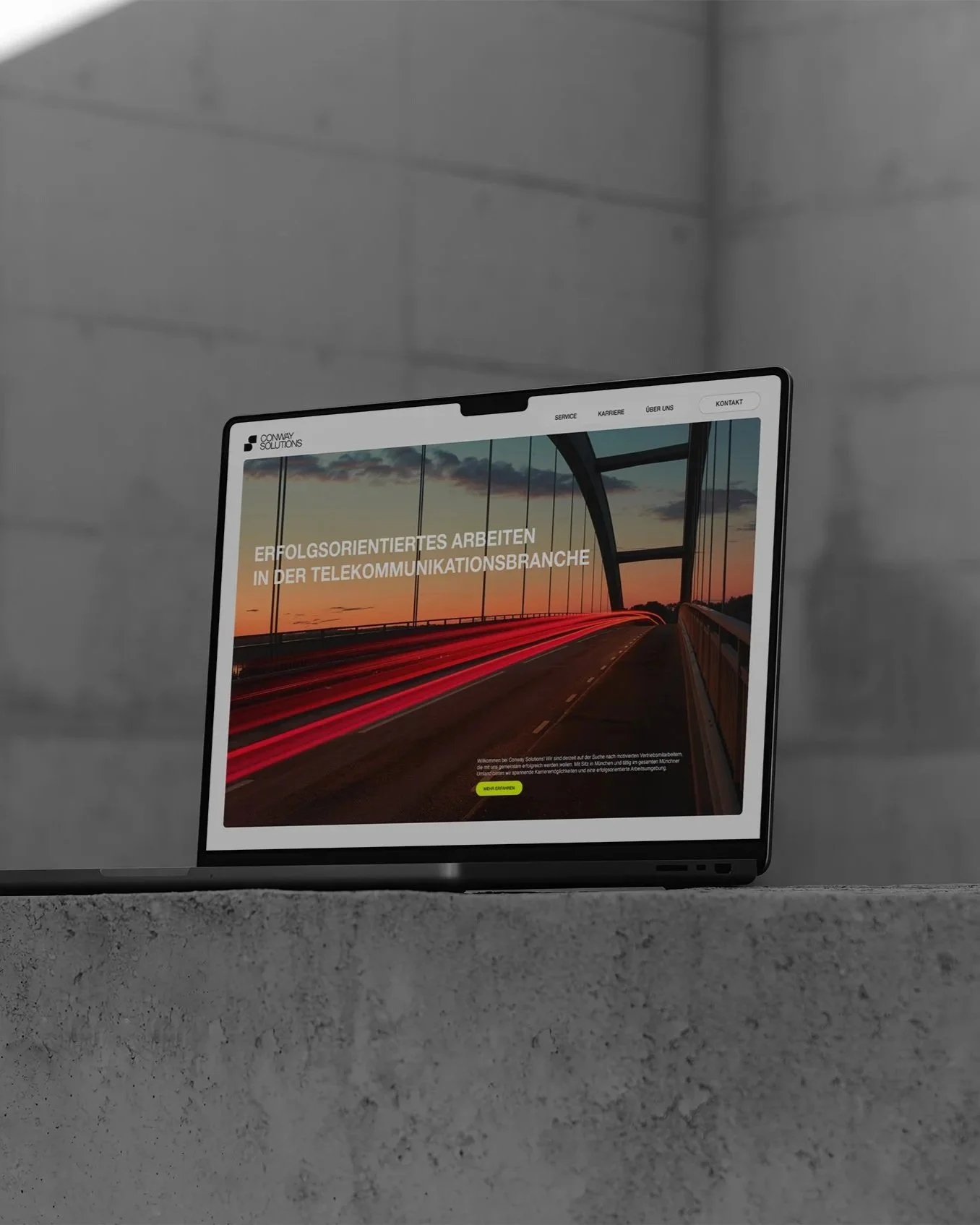 Ein Laptop auf einer Betonoberfläche zeigt eine Website für Conway Solutions, die sich auf Telekommunikationsbranche spezialisiert hat. Die Website hat ein Bild einer Brücke bei Sonnenuntergang mit roten Lichtspuren auf der Straße.