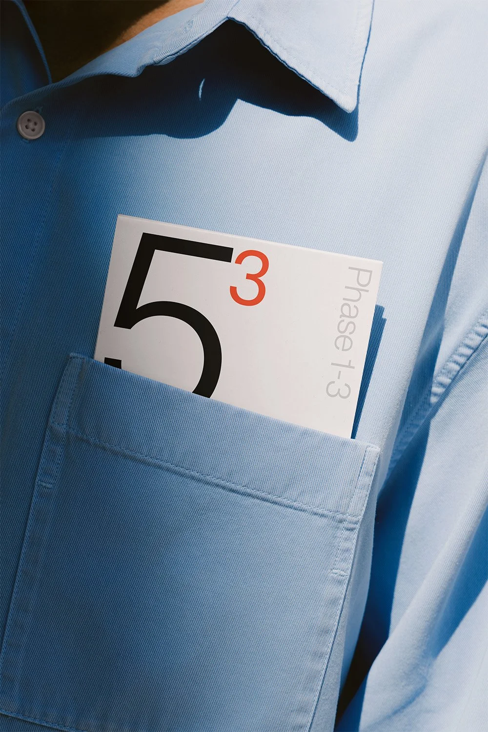 Ein Mann trägt ein hellblaues Hemd, in der Brusttasche steckt eine Wartelisten-Nummer mit der Nummer 535, darunter die Nummer 3 in rot.