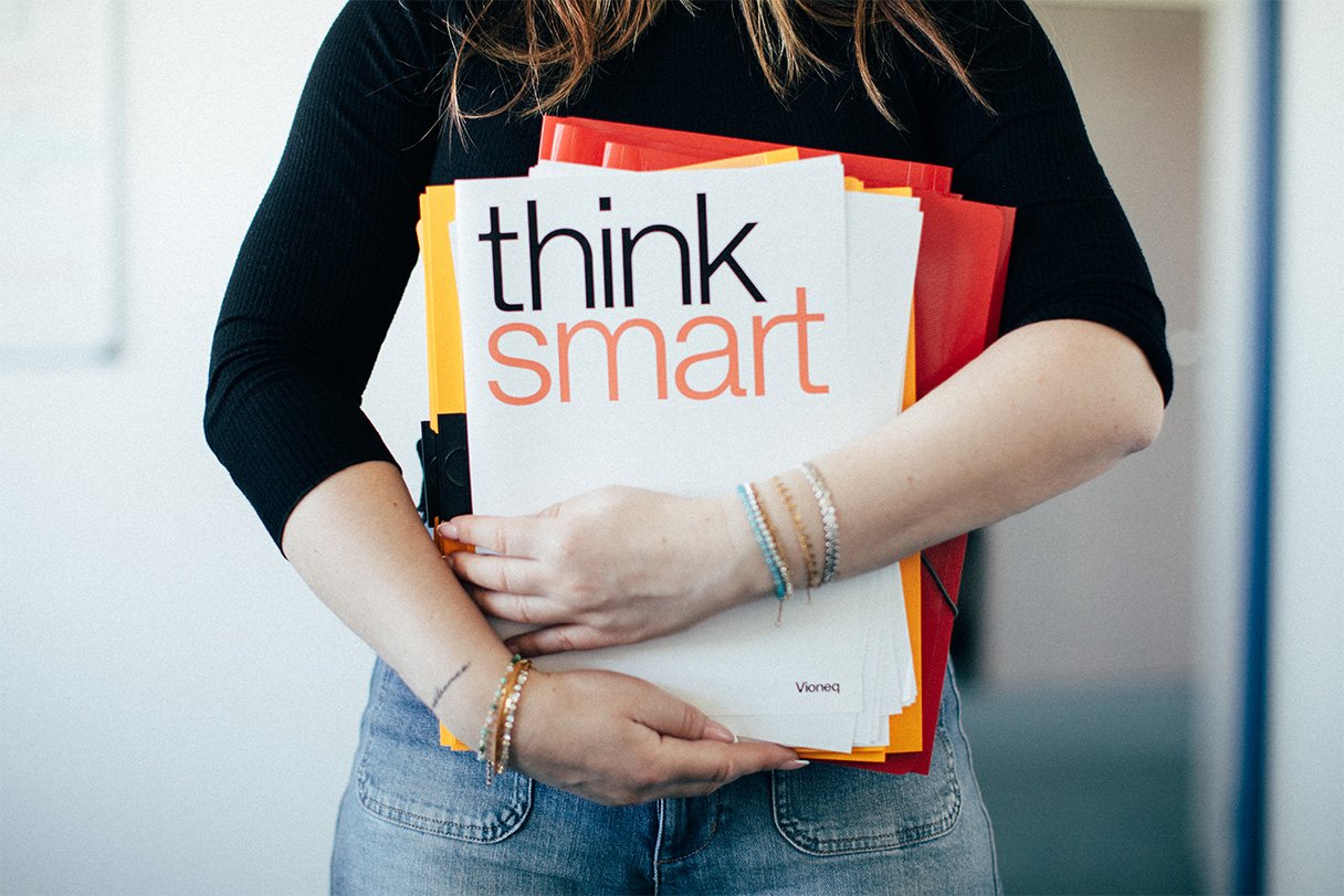 Eine Person hält mehrere gestapelte Bücher mit dem Titel "think smart" in den Armen.