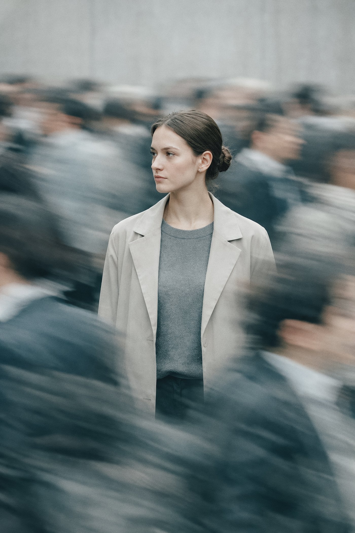 Eine junge Frau mit dunkelbraunem Haar, die inmitten einer Menschenmenge steht und nach vorne blickt, während die Menschen um sie herum in Bewegung sind.