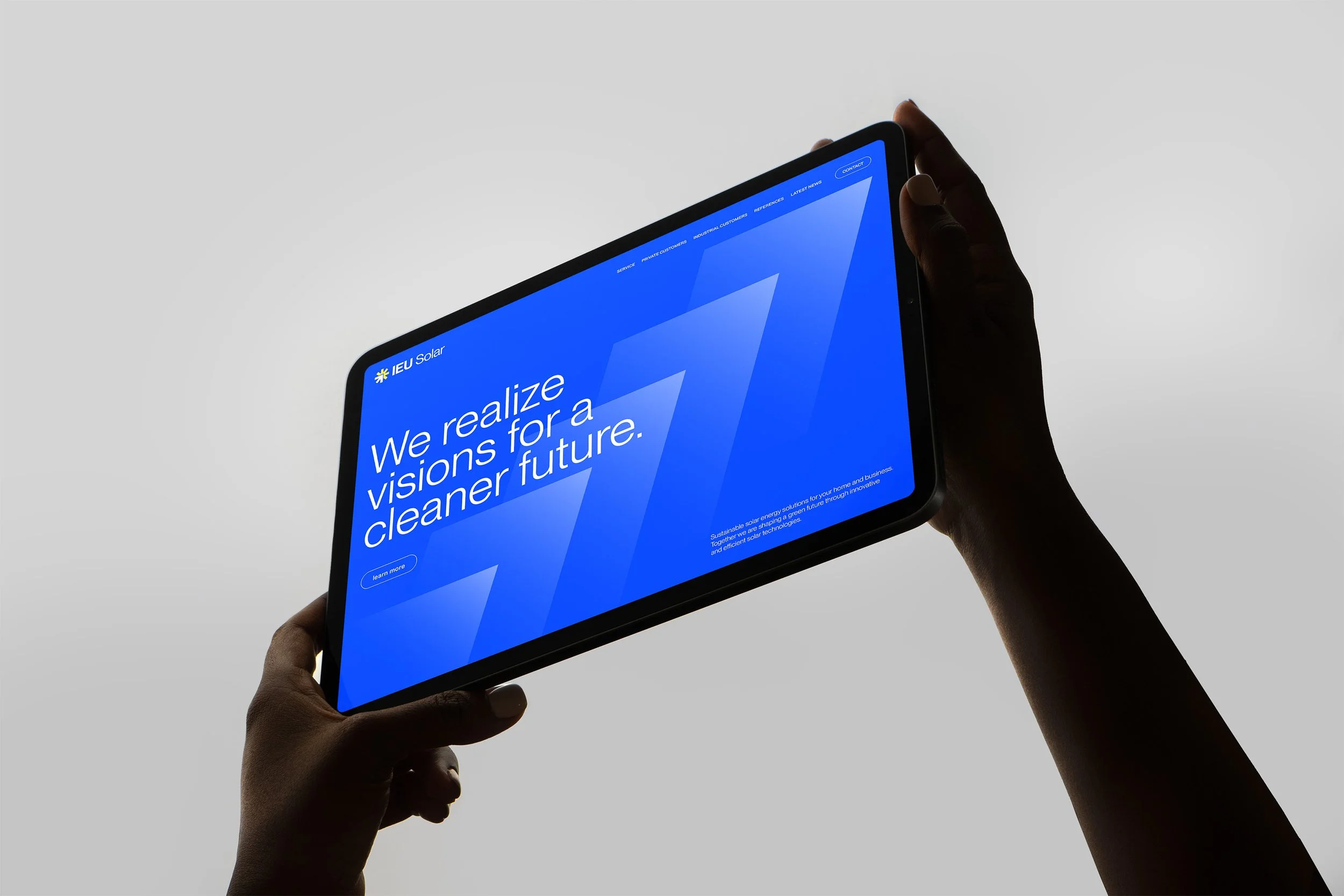 Eine Person hält ein Tablet in der Hand, auf dem eine Webseite mit blauer Hintergrundfarbe und weißem Text sichtbar ist. Es ist eine Botschaft über Solarenergie und eine nachhaltige Zukunft zu sehen.