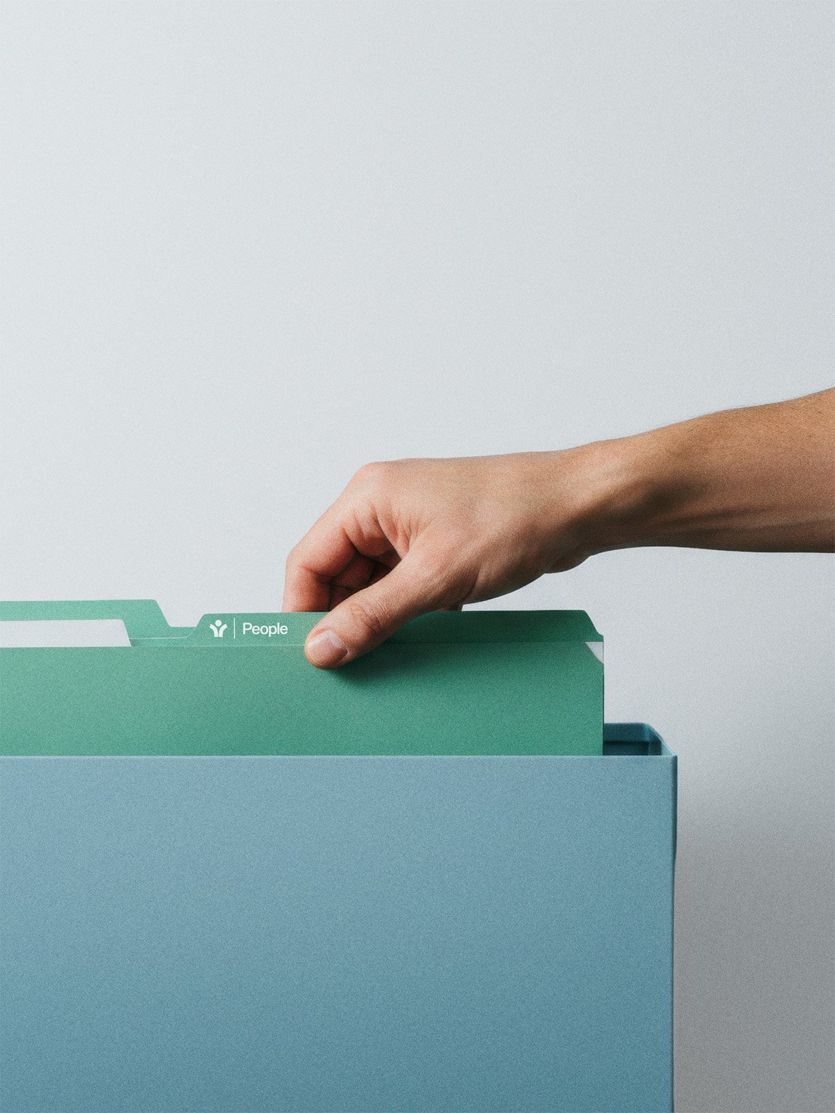 Nahaufnahme einer Hand, die eine Aktenmappe in einer hellblauen Ablage mit weiteren Aktenordnern steckt, der Ordner ist grün mit einem weißen Etikett mit der Aufschrift 'People'.