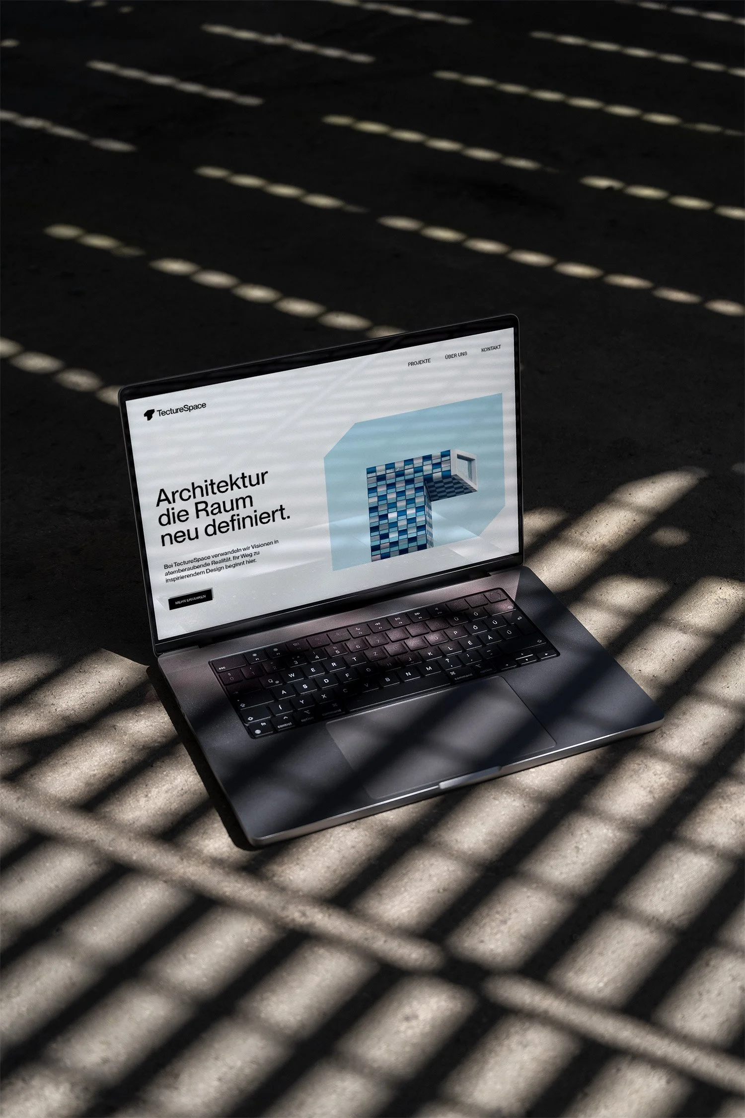 Auf einem Laptop-Bildschirm ist eine Webseite mit dem Titel 'Architektur die Raum neu definiert' zu sehen, im Hintergrund schwarze Oberfläche mit Schatten von Gitternetzlinien.