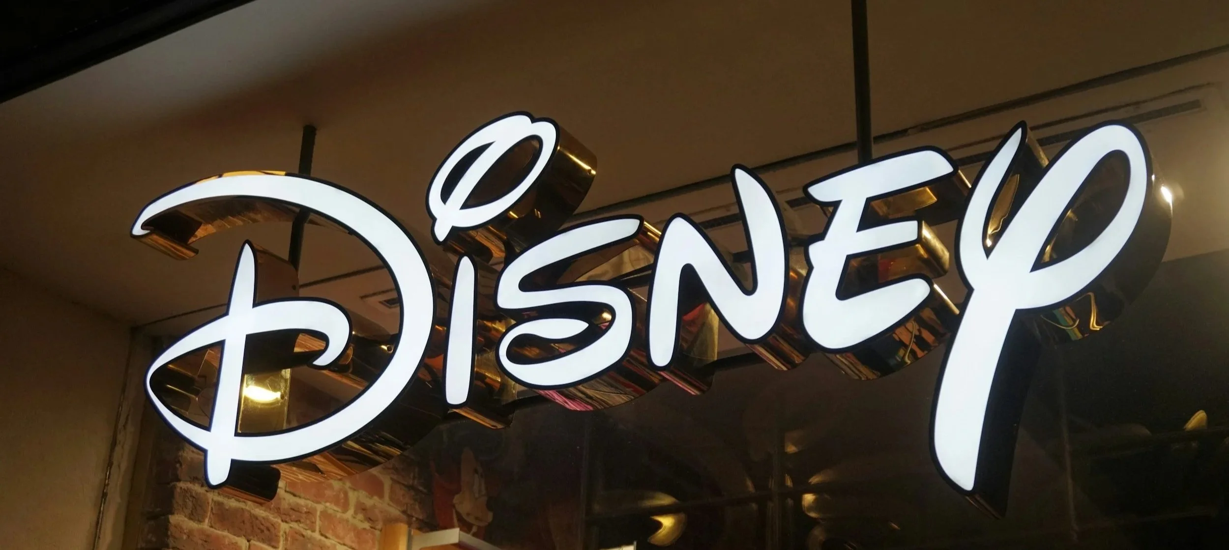 Illuminated Disney sign in black and white lettering on a wall with exposed brick.