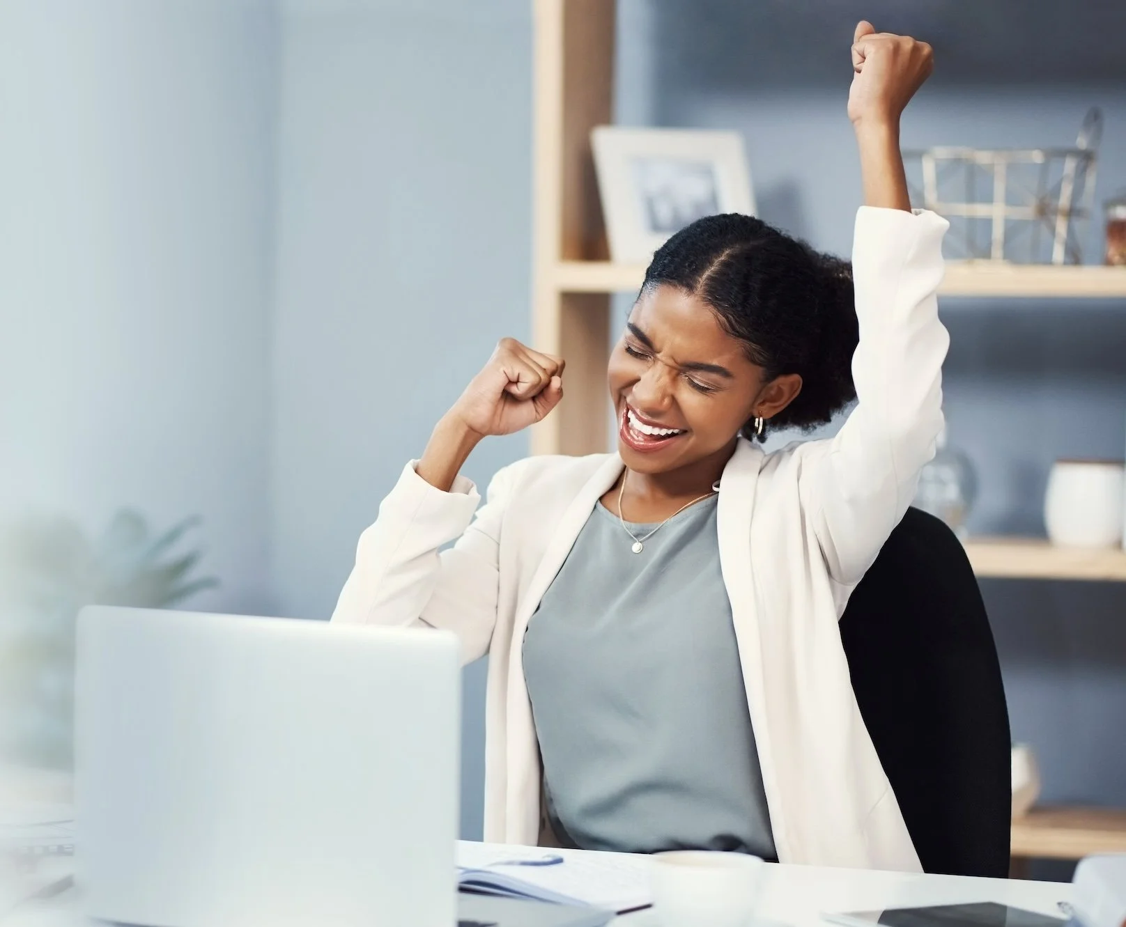 woman sitting at a desk in front of her computer pumping her fist in the air