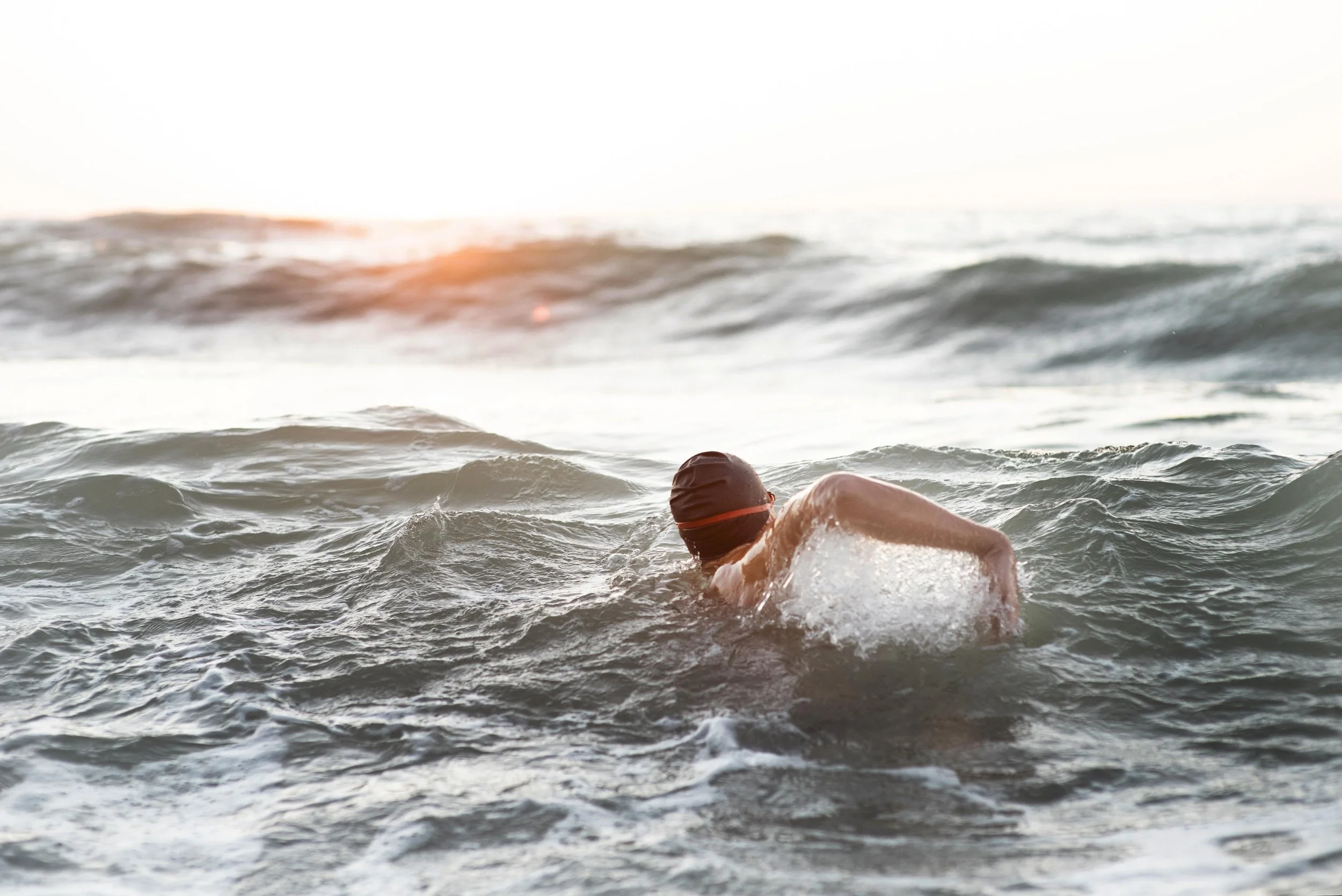 Person swimming in the ocean at sunset, wearing a swim cap