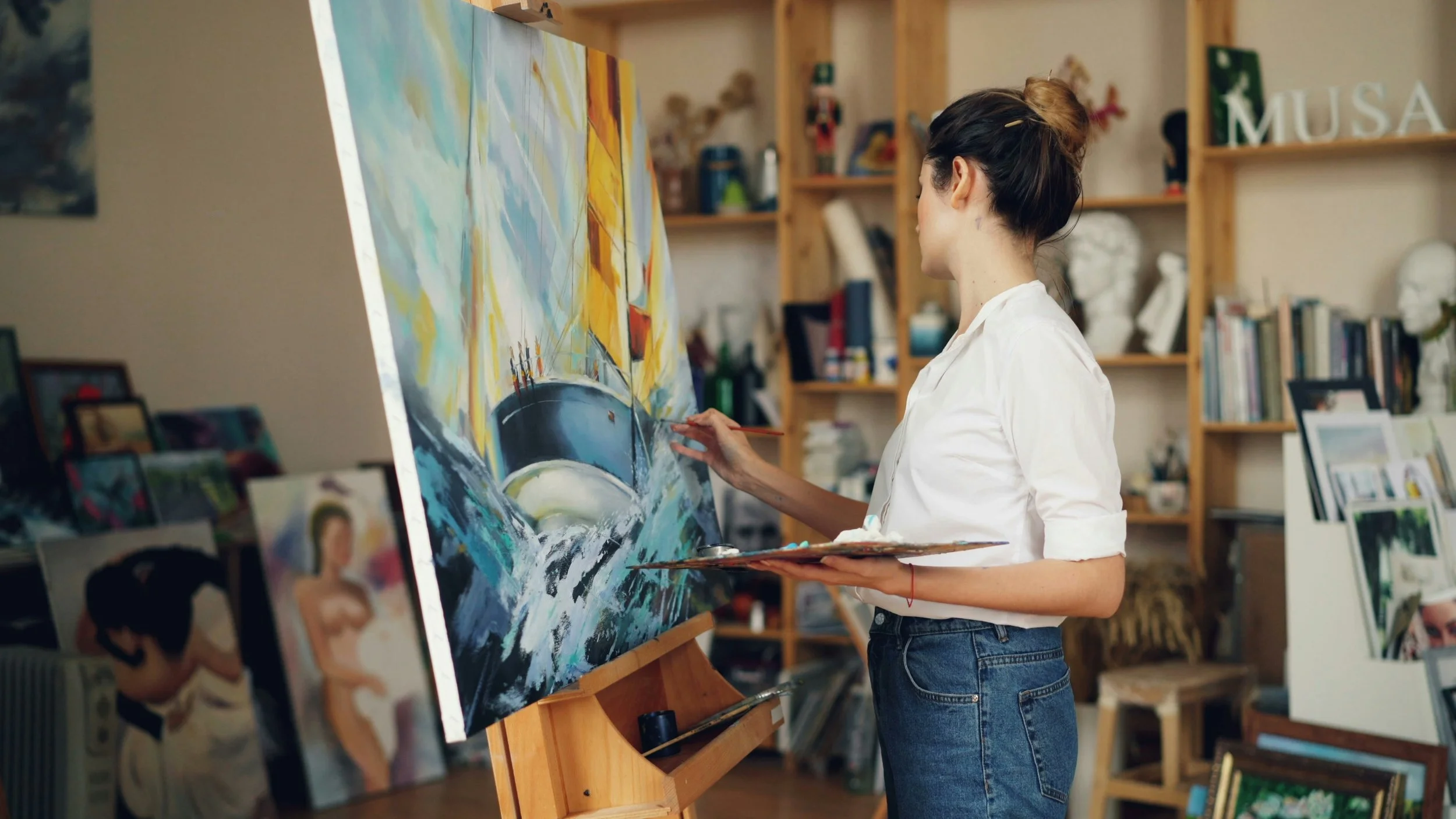 Female artist in bright studio holding paintbrush and palette, reflecting on the creative process and what defines true art.