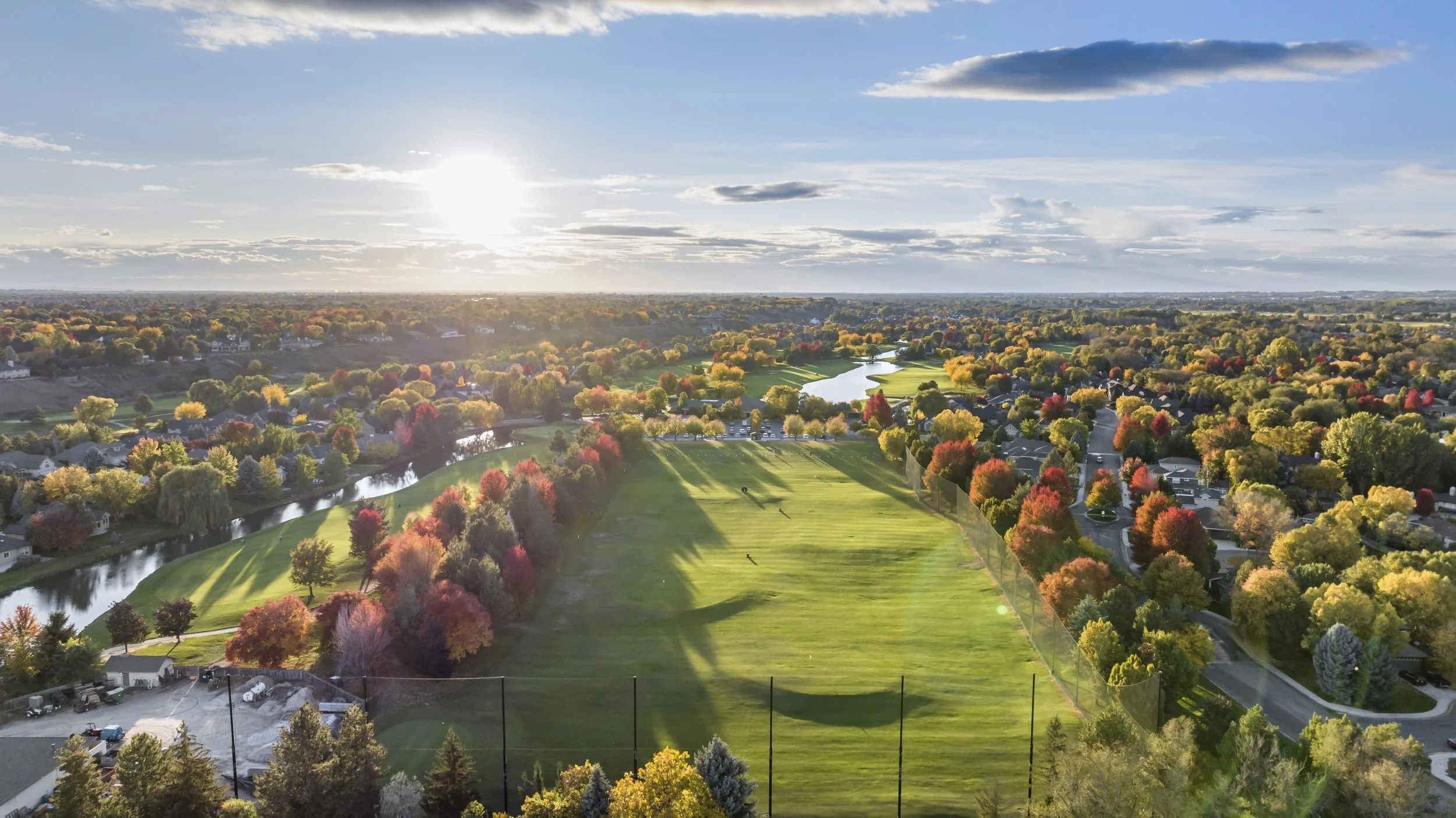 Aerial view of an Eagle, Idaho golf course with neatly trimmed greens, surrounded by houses, the Boise River, and a neighborhood with roads on a sunny day.