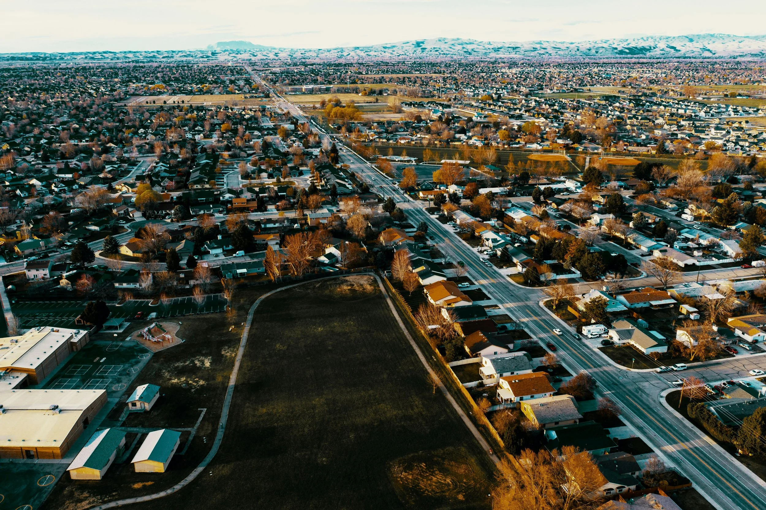 A suburban Meridian neighborhood with single-family homes, trees, roads, and a park, with the Boise foothills in the background.