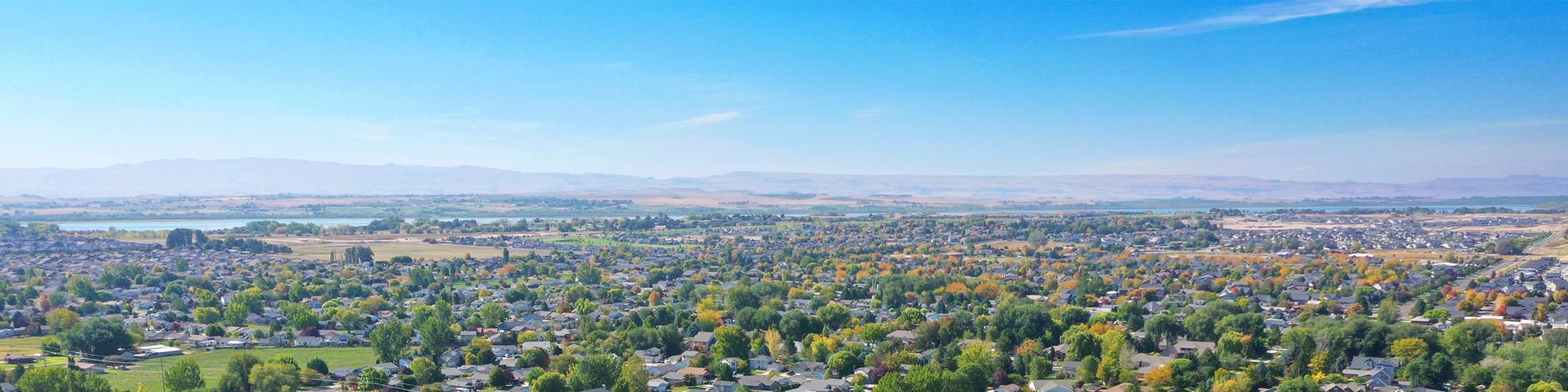 A wide view of a suburban Boise cityscape with numerous houses, trees, and streets, with Boise Foothills in the background.