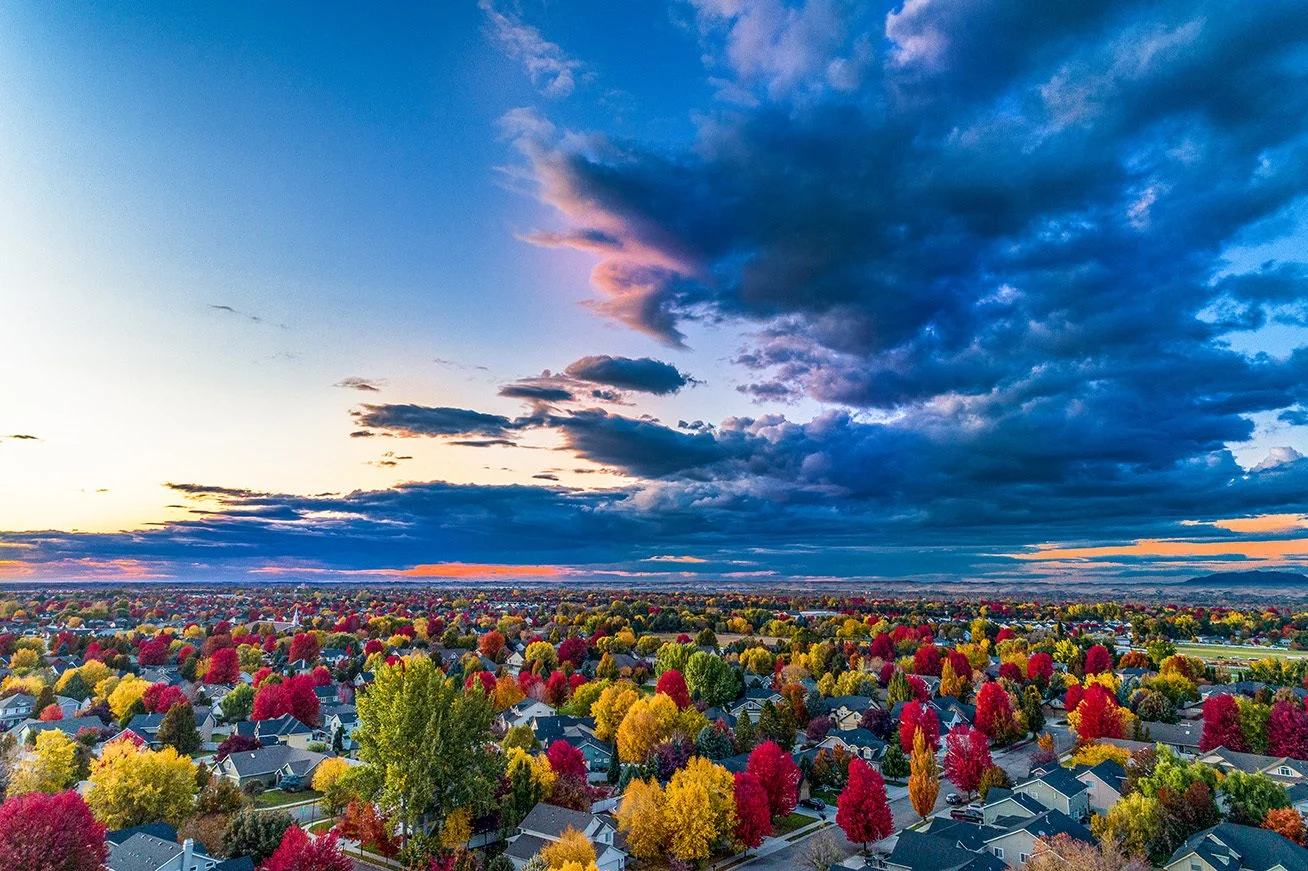 Aerial view of a suburban neighborhood with colorful fall trees and a partly cloudy sky at sunset.