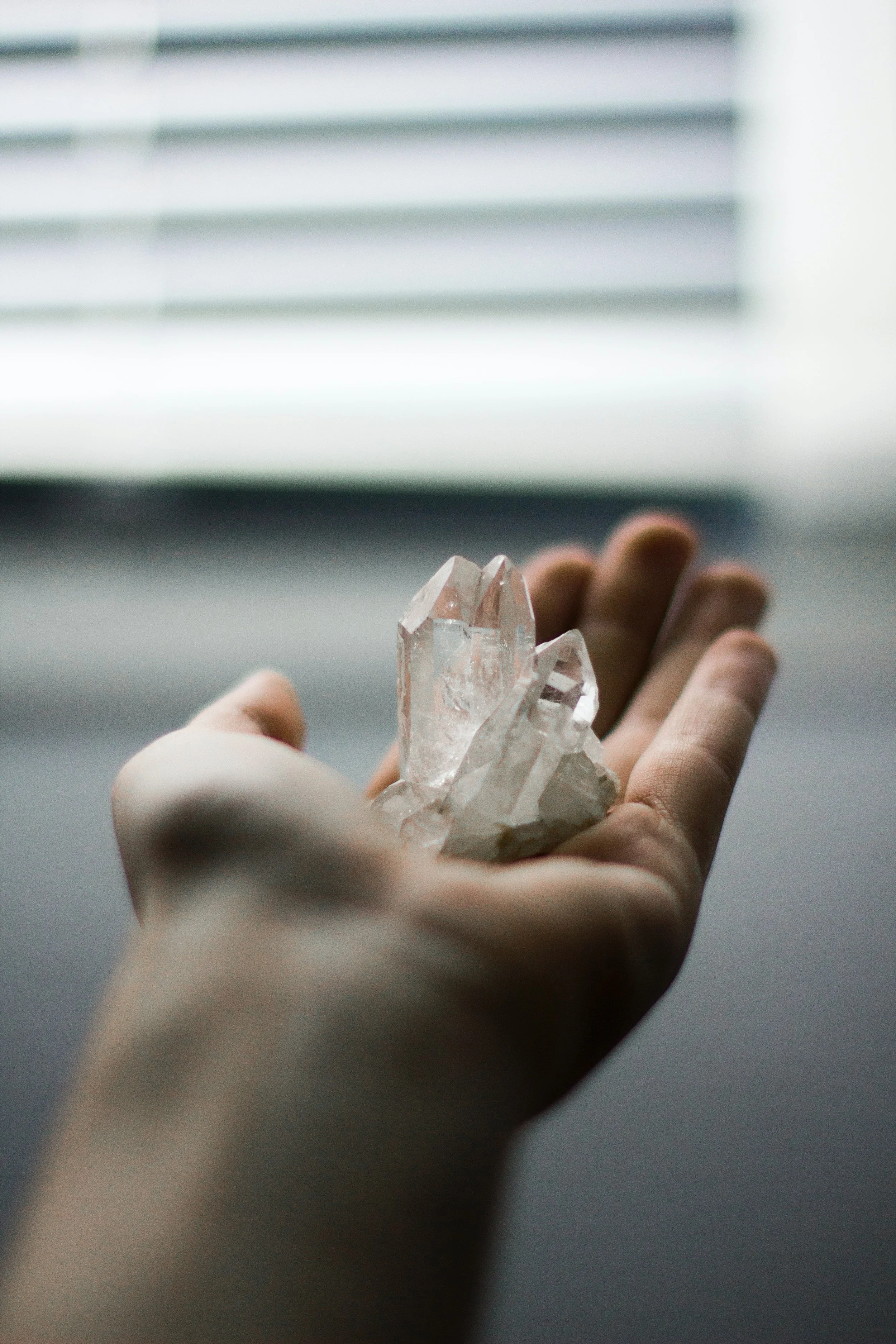 Person holding a clear quartz crystal near a window with blinds.