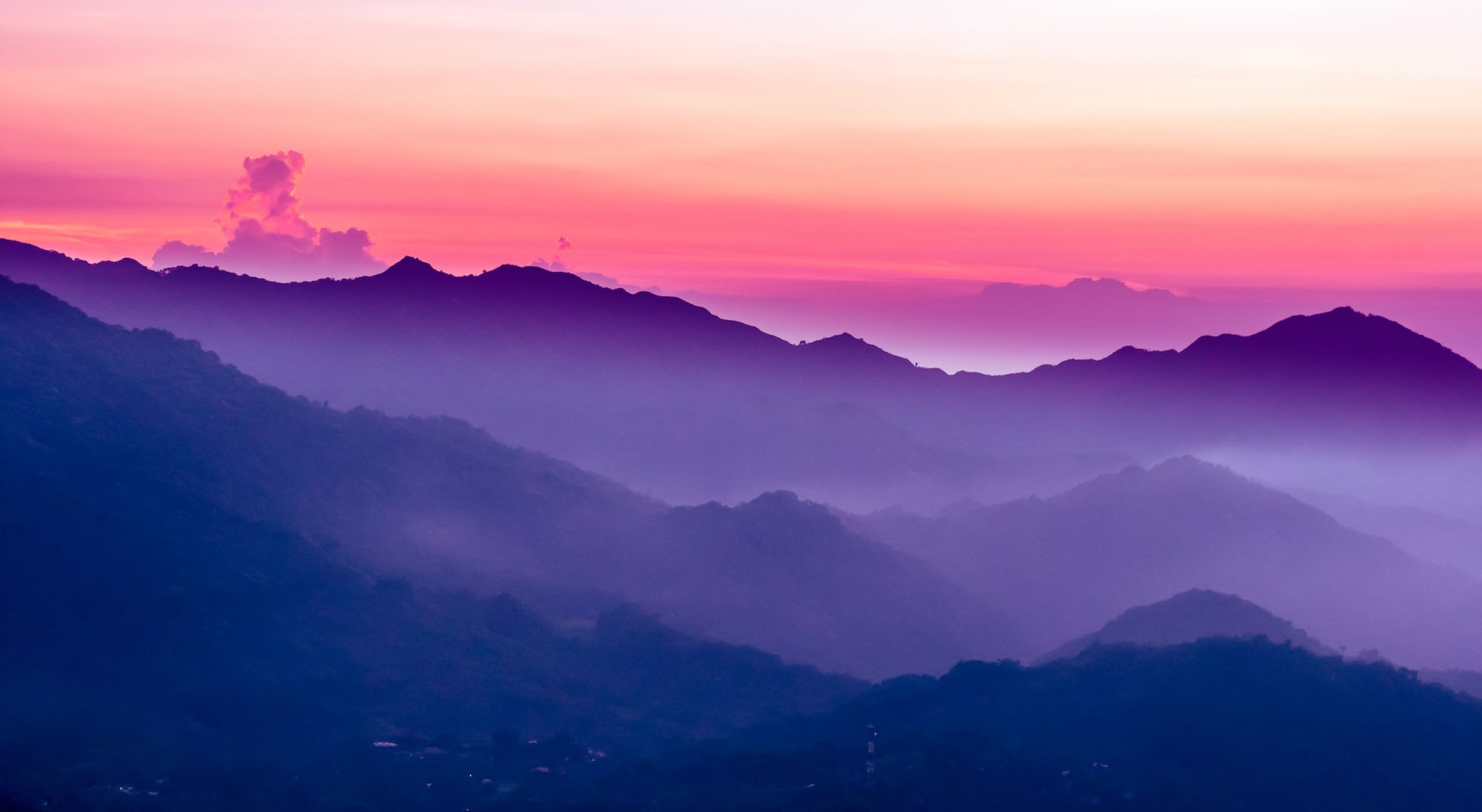 Colorful mountain landscape at sunset with pink, purple, and blue sky and layered mountain ridges.
