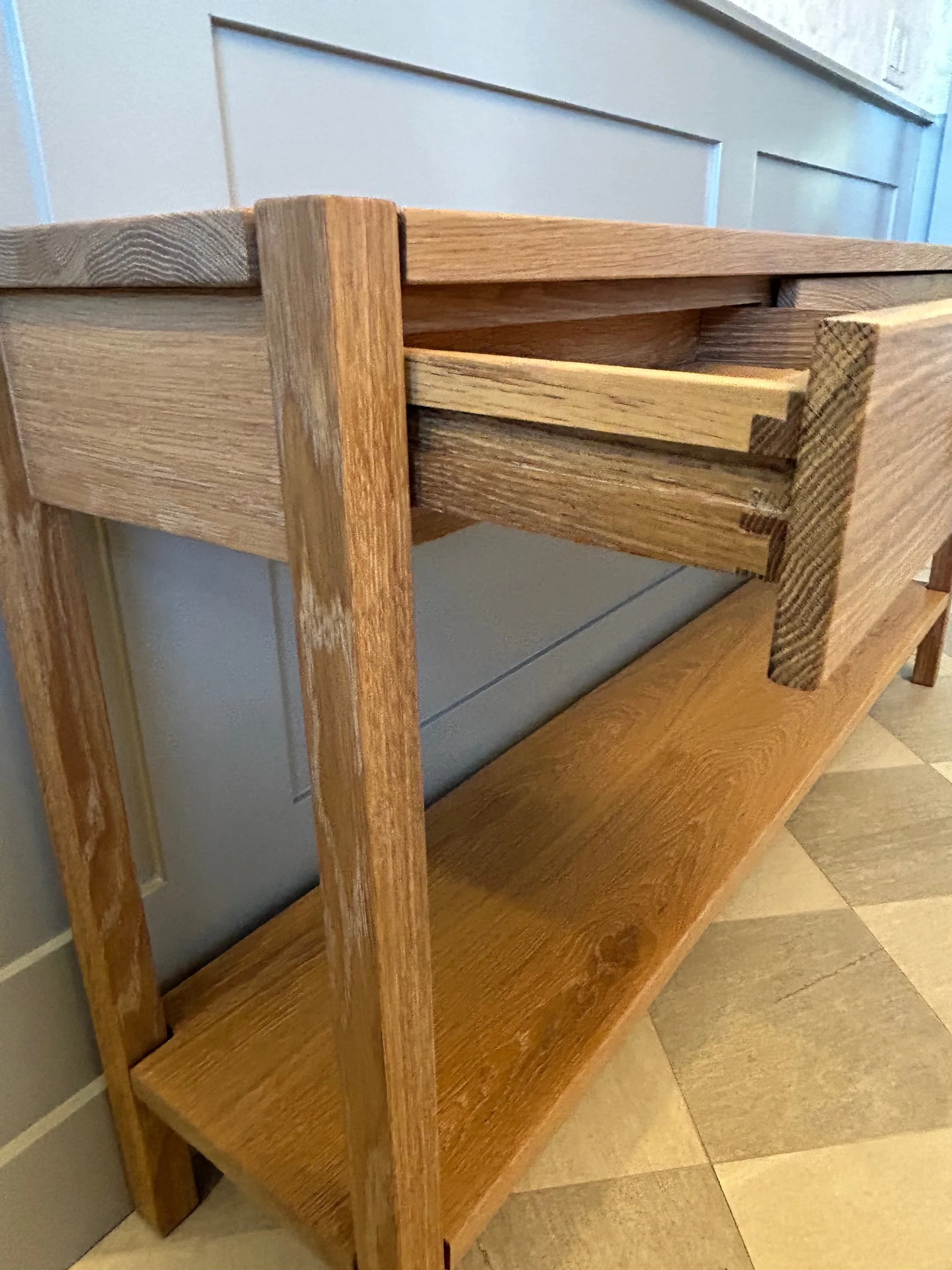 A wooden sideboard with an open and a closed drawer, showing my hand slipping it out, placed on a tiled floor against a wall.