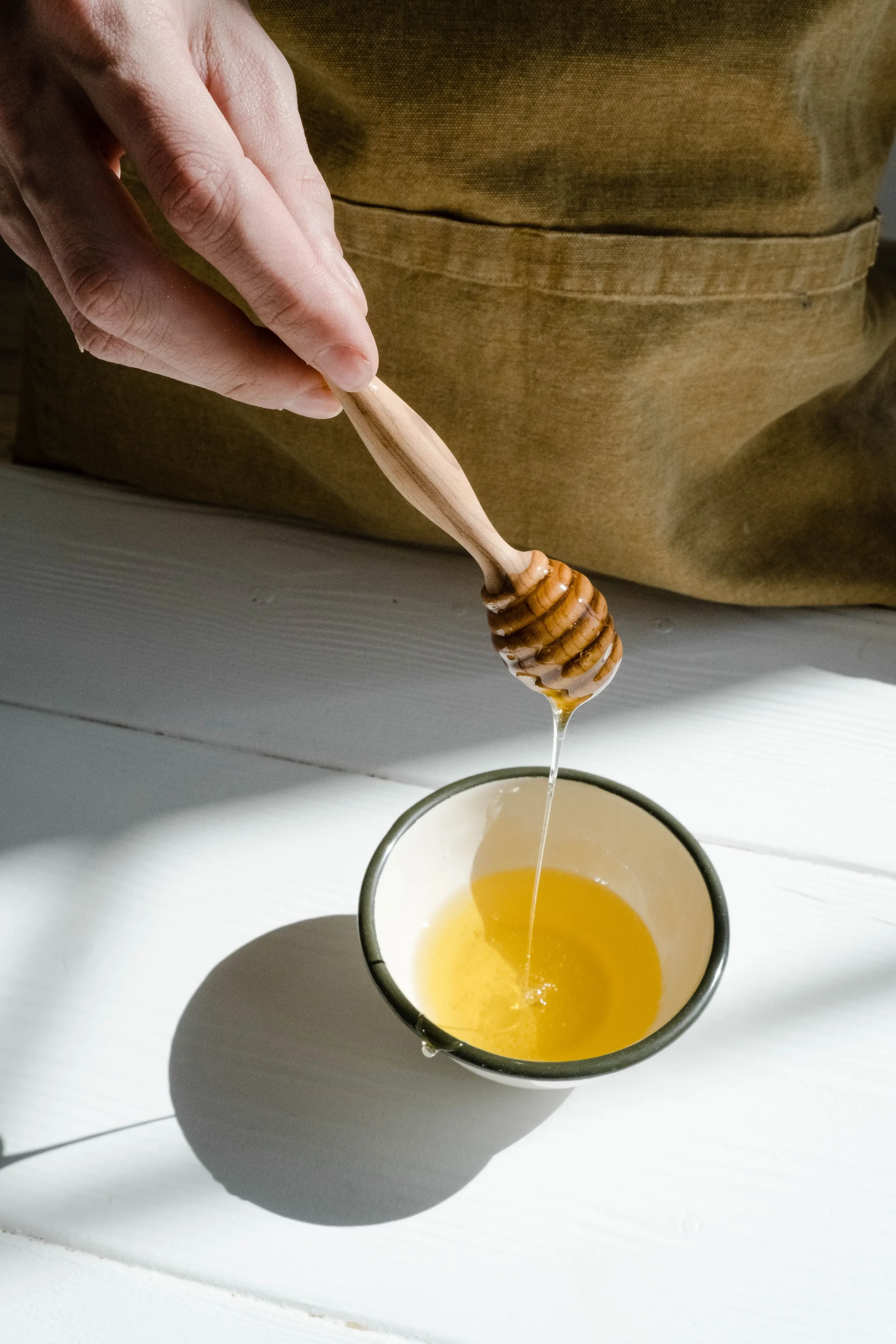 Person drizzling natural raw honey into a small bowl with a wooden honey dipper