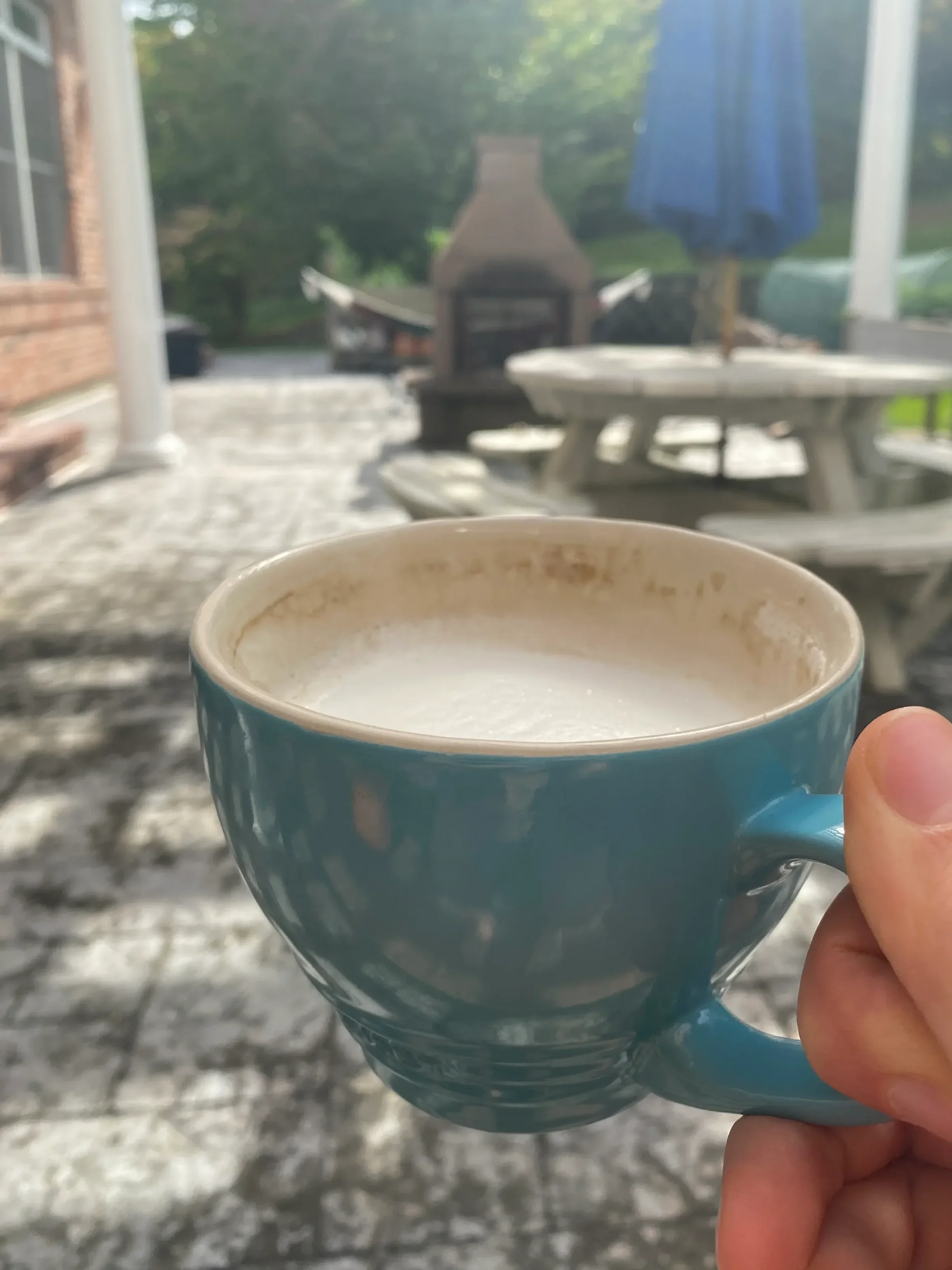 A person holding a teal cup of frothy herbal latte on a sunny outdoor patio, representing the mindful morning rituals and stress management coaching at Holistus Health.
