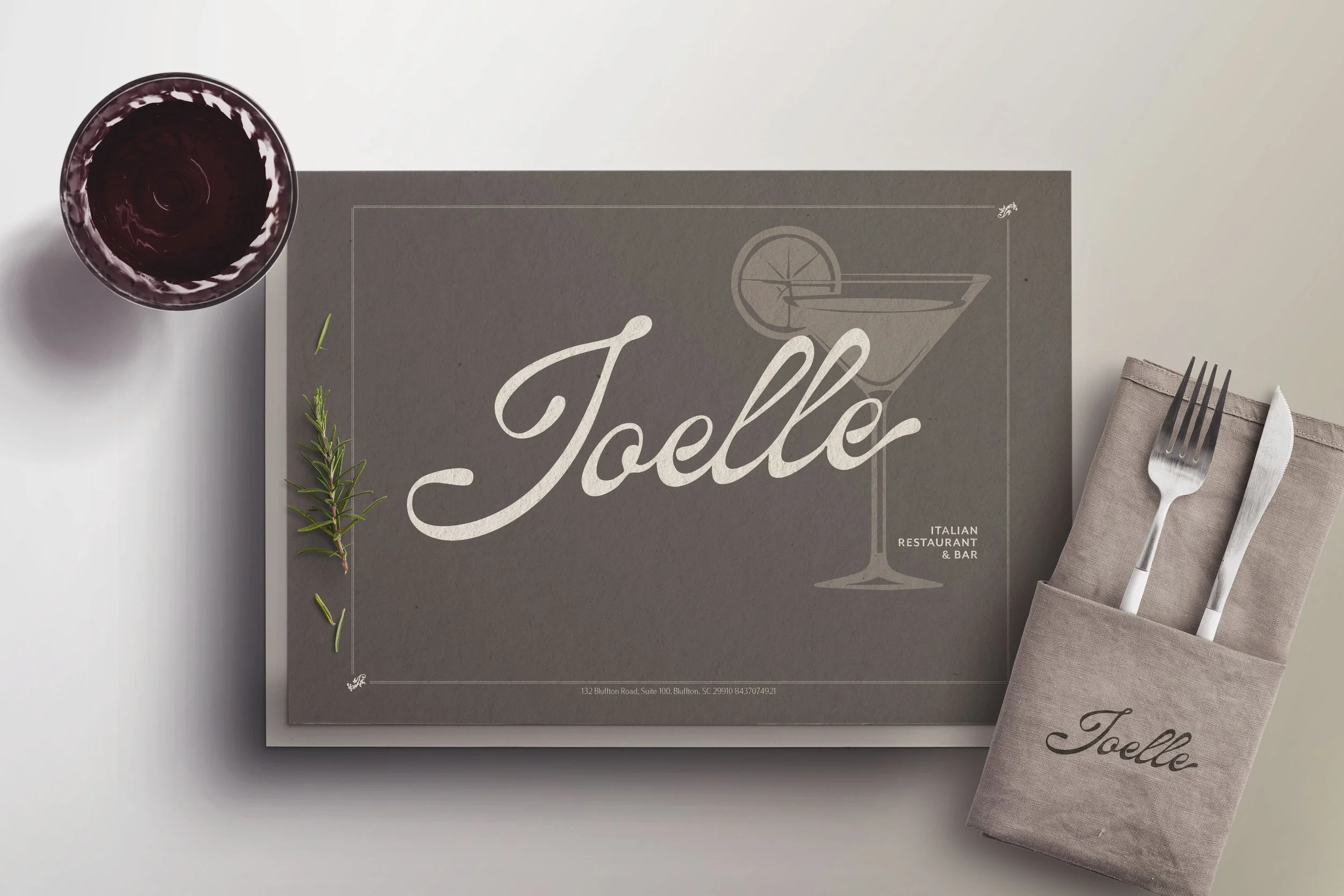 A restaurant menu titled 'Joelle' with a graphic of a cocktail glass, a sprig of rosemary, a glass of red wine, and a utensil set on a napkin with the restaurant's name, 'Joelle', printed on it.