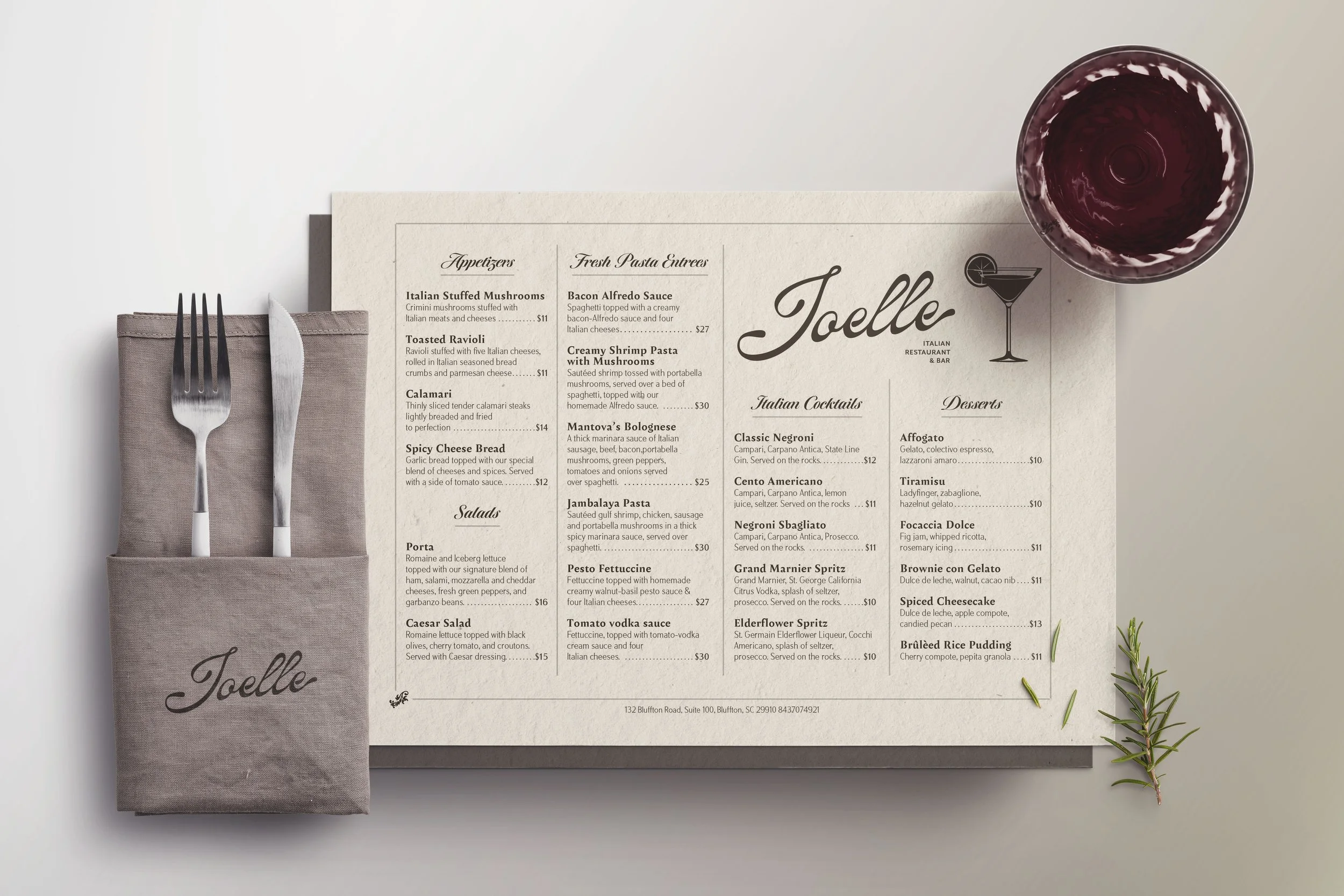 A restaurant menu from Joelle Italian Restaurant and Bar, with sections for appetizers, salads, pasta entrees, Italian cocktails, and desserts, a glass of red wine, a fork and knife on a napkin, and a sprig of rosemary.