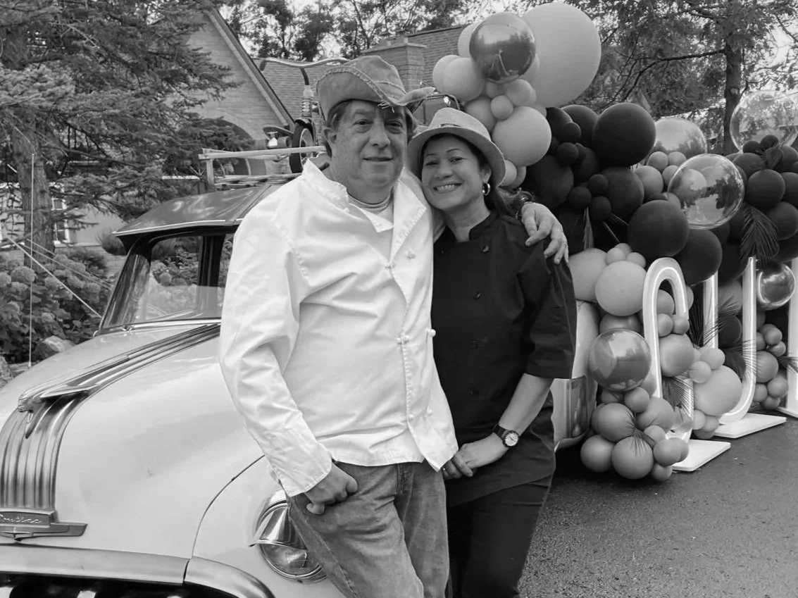 Chef Chuchi  and Patty standing close together in front of a vintage car and decorative balloons.