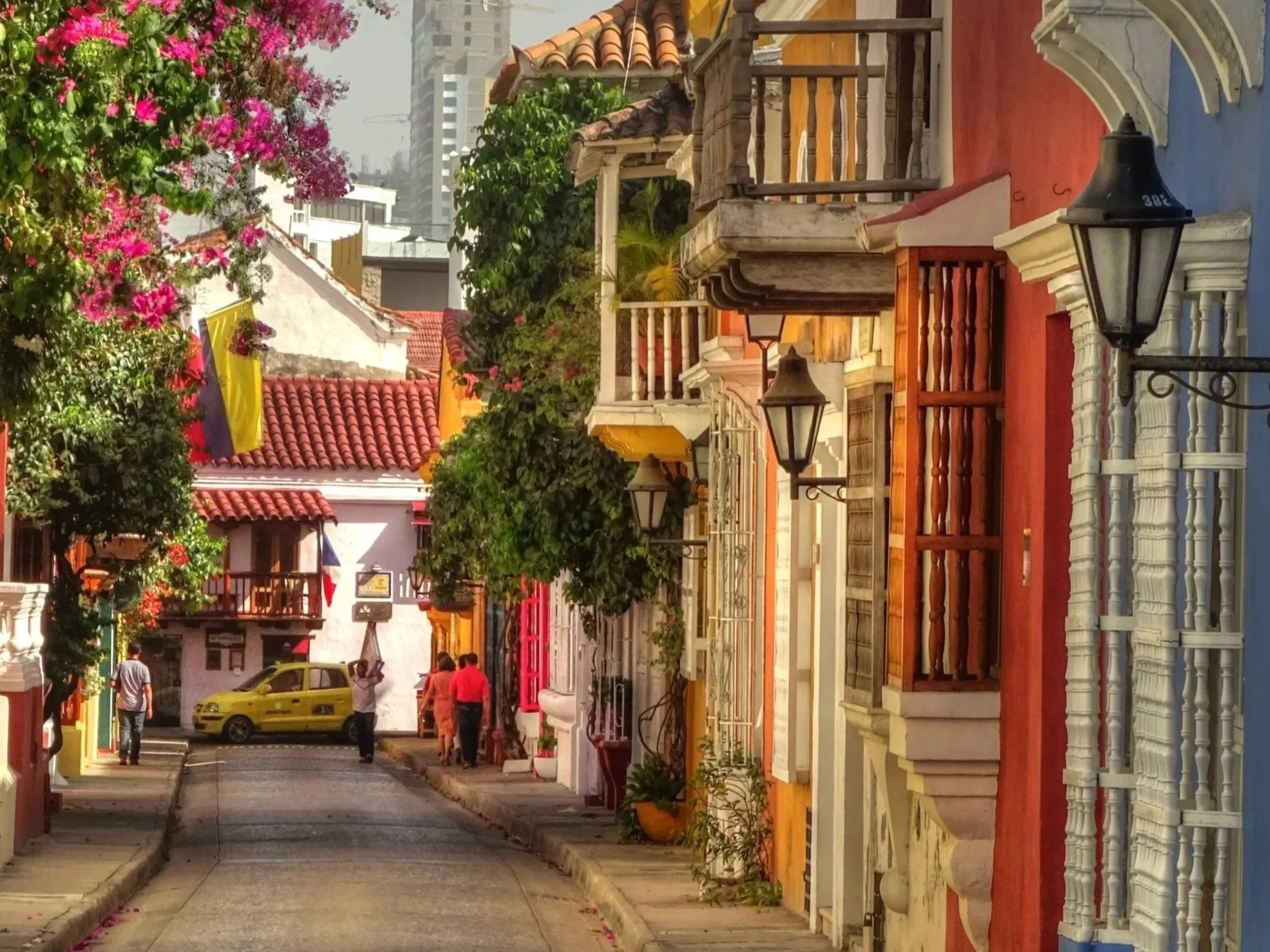 A historic street in a Latin American town with colorful buildings, balconies, and a church tower in the background.
