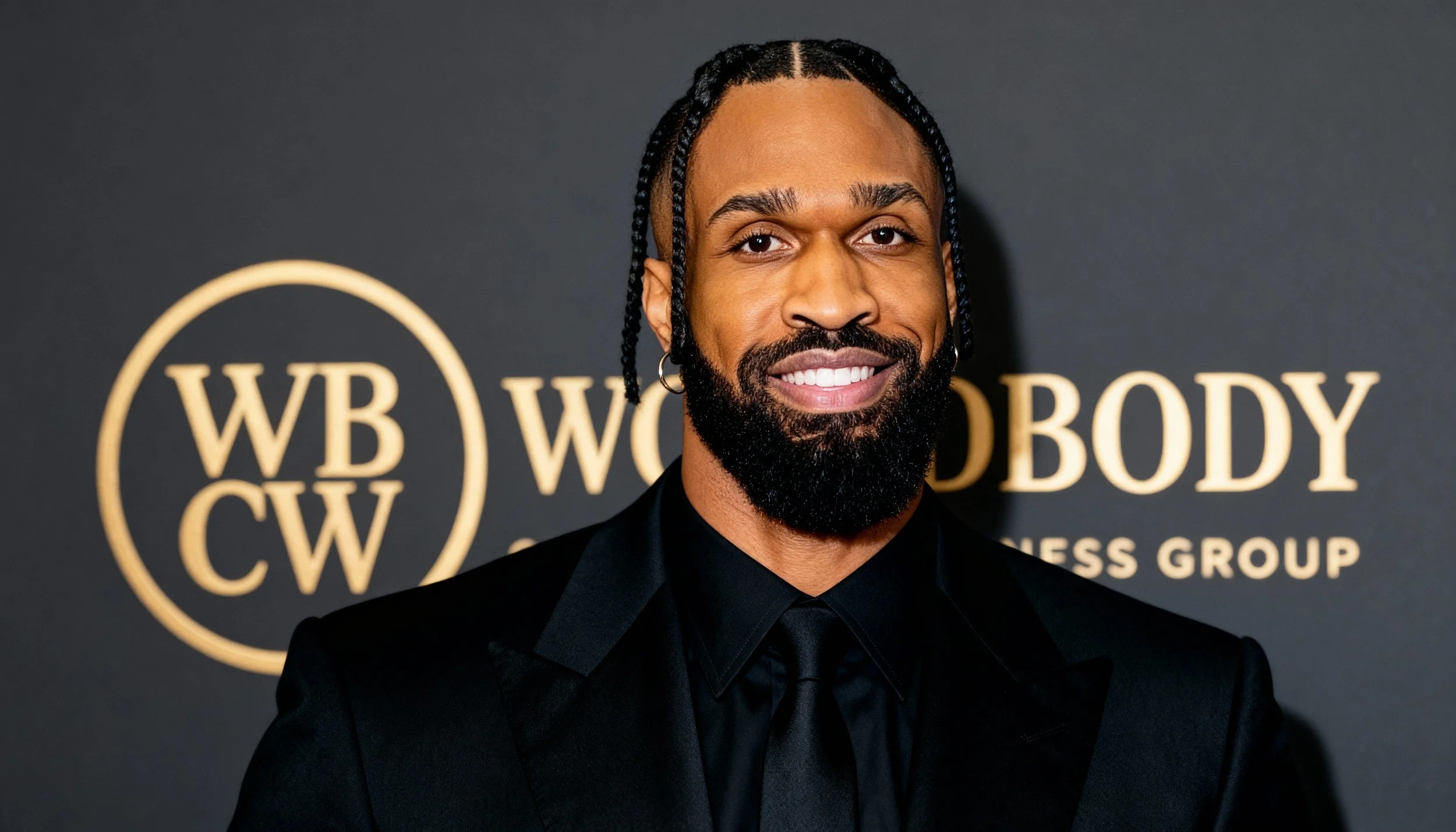 A man in a pink suit talking on his cell phone next to a black luxury sports car with gull-wing doors, parked on a city street with palm trees and buildings in the background during sunset.