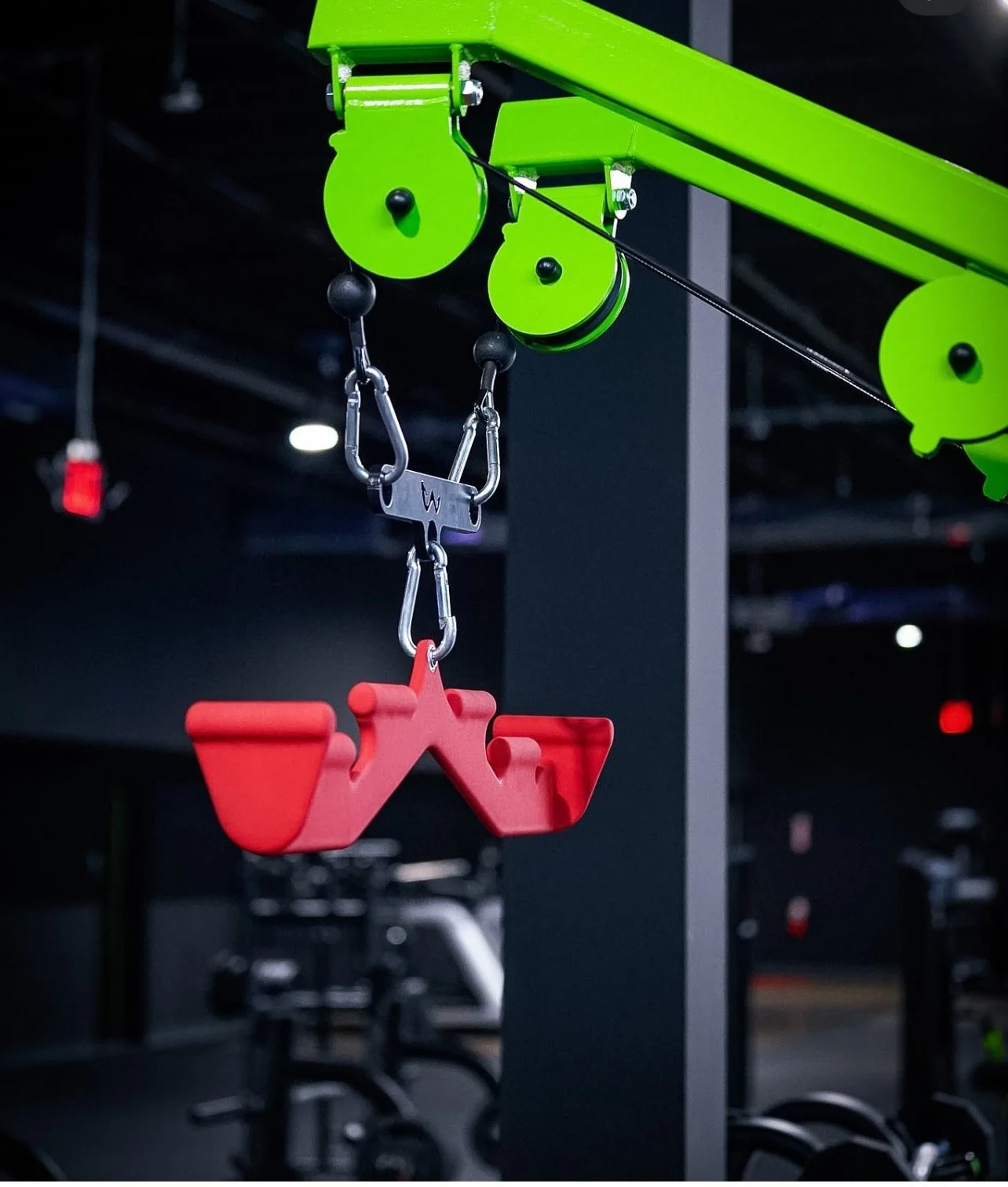 Close-up of a red gym chalk holder hanging from a green gym equipment pully system in a gym.