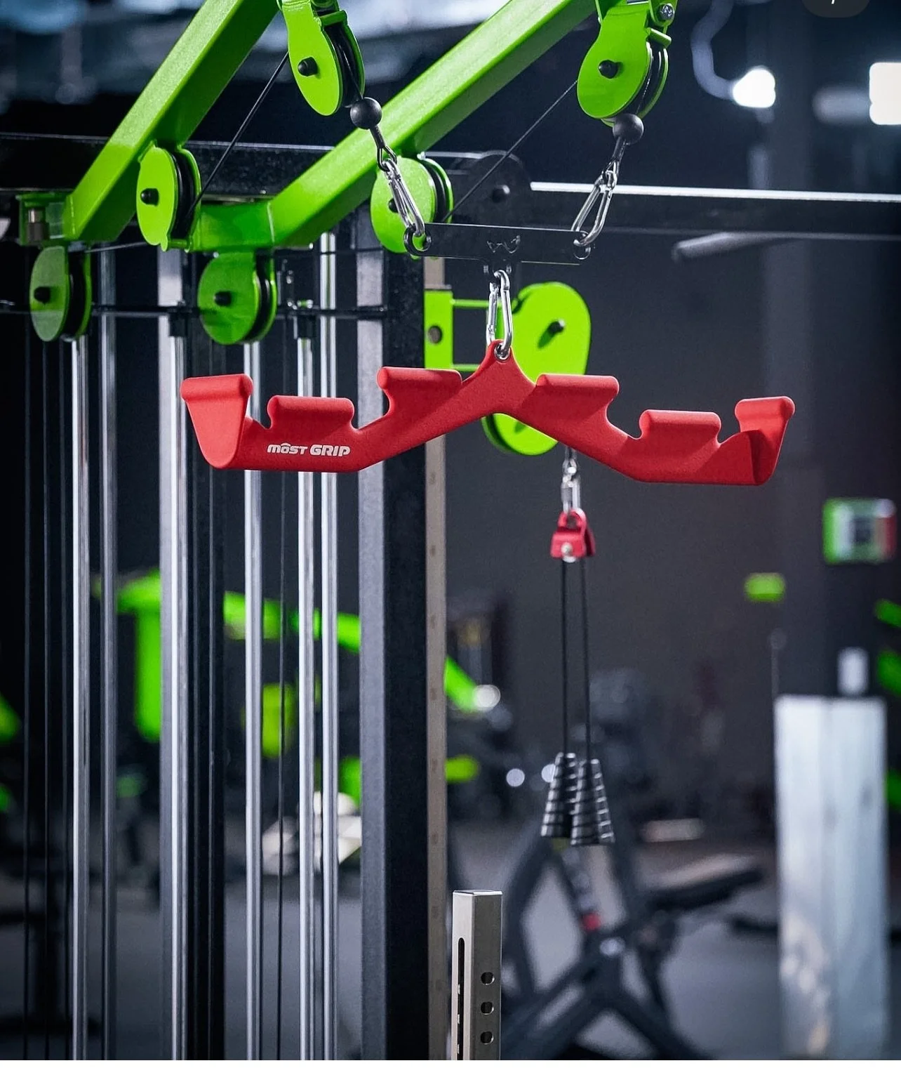 A red grip attachment hanging from a workout machine in a gym, with green workout equipment visible in the background.