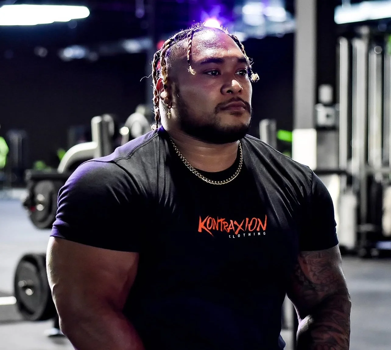 Person hanging upside down on a green and yellow fitness frame in a gym, with black leggings and gloves, surrounded by colorful exercise equipment.