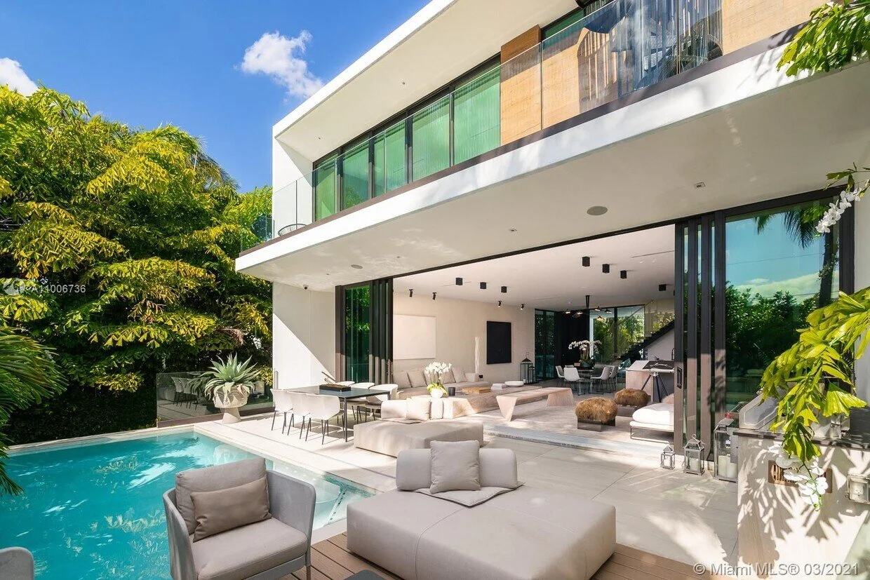 Modern house with an outdoor swimming pool, white lounge chairs, and an open living area with white furniture and large sliding glass doors