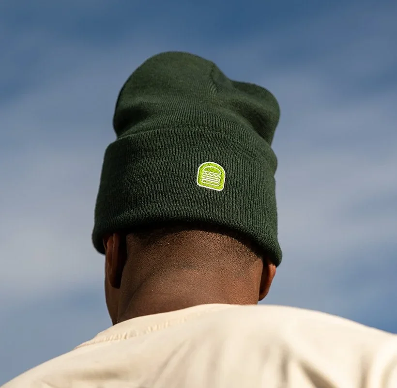 Back of a person wearing a dark green beanie with a small rectangular logo, facing away against a partly cloudy sky.