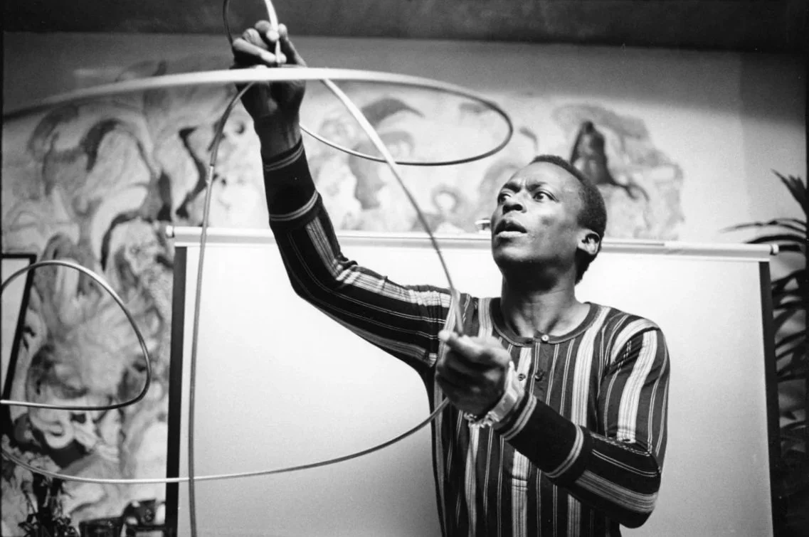 A man holding and arranging wire sculptures, with a mural in the background.