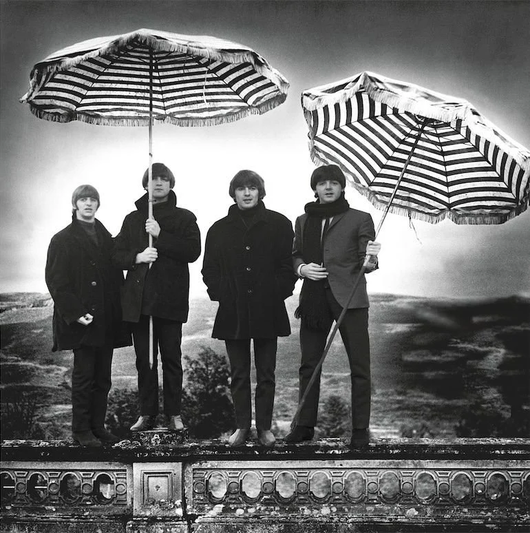 The Beatles photographed by Robert Whitaker, standing under striped umbrellas in a black-and-white outdoor portrait, available as a fine art print at Modern Rocks Gallery.