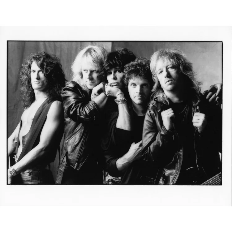 Black and white photo of five rock band members posing with serious expressions, wearing leather jackets and casual clothing.