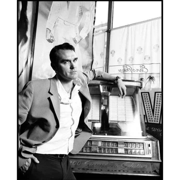 A man in a suit leaning against a jukebox in a retro-style setting, with a large poster of a boxer in the background.
