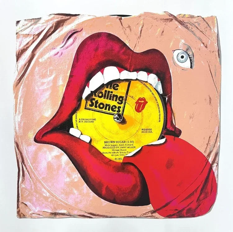 Artwork of a large open mouth with red lips and white teeth, holding a yellow vinyl record inside the mouth with the label 'The Rolling Stones'. The tongue is sticking out and holding a red lipstick. One eye is visible above the lips.