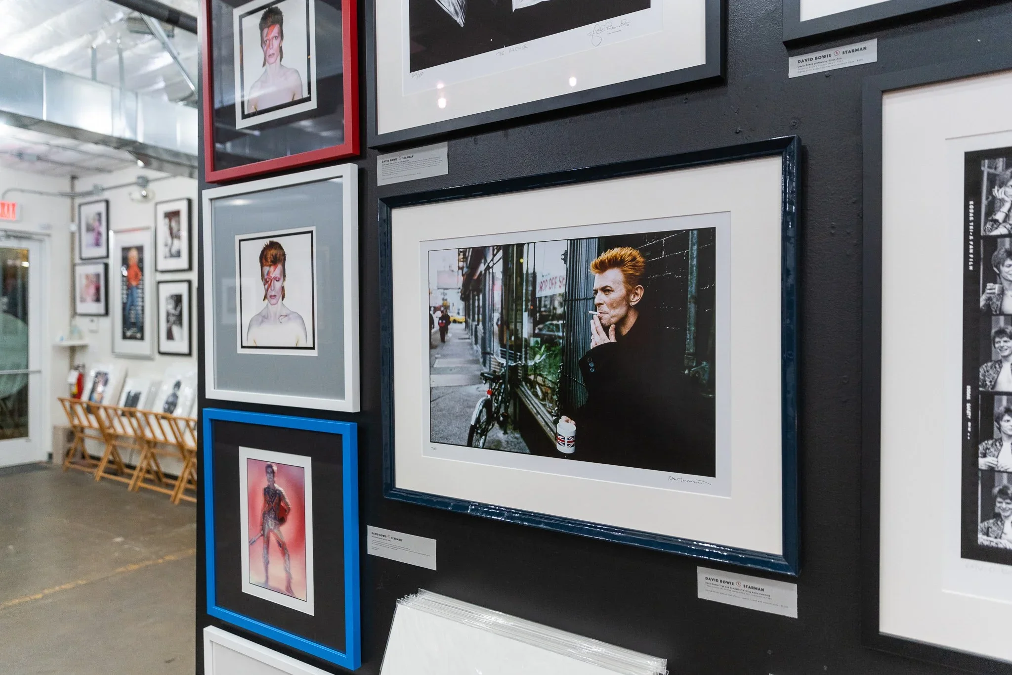 Gallery wall featuring framed photographs including a man with reddish hair smoking on a city street, styled portraits of a woman with short hair and glasses, and other mixed photographs.
